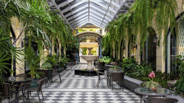 A checkered floor with tables and chairs, a central fountain, and lush greenery in a covered outdoor area. - The Sukosol (Bangkok)