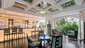 A spacious bar area with high ceilings, multiple seating arrangements, and a view of greenery outside. - The Sukosol (Bangkok)