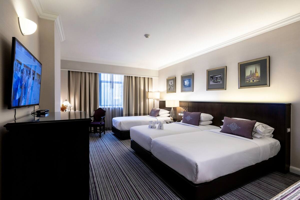 A hotel room with two beds, a desk, a television, and a window with curtains.