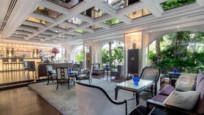 A spacious living area with a high ceiling, large windows, and a view of lush greenery outside. - The Sukosol (Bangkok)