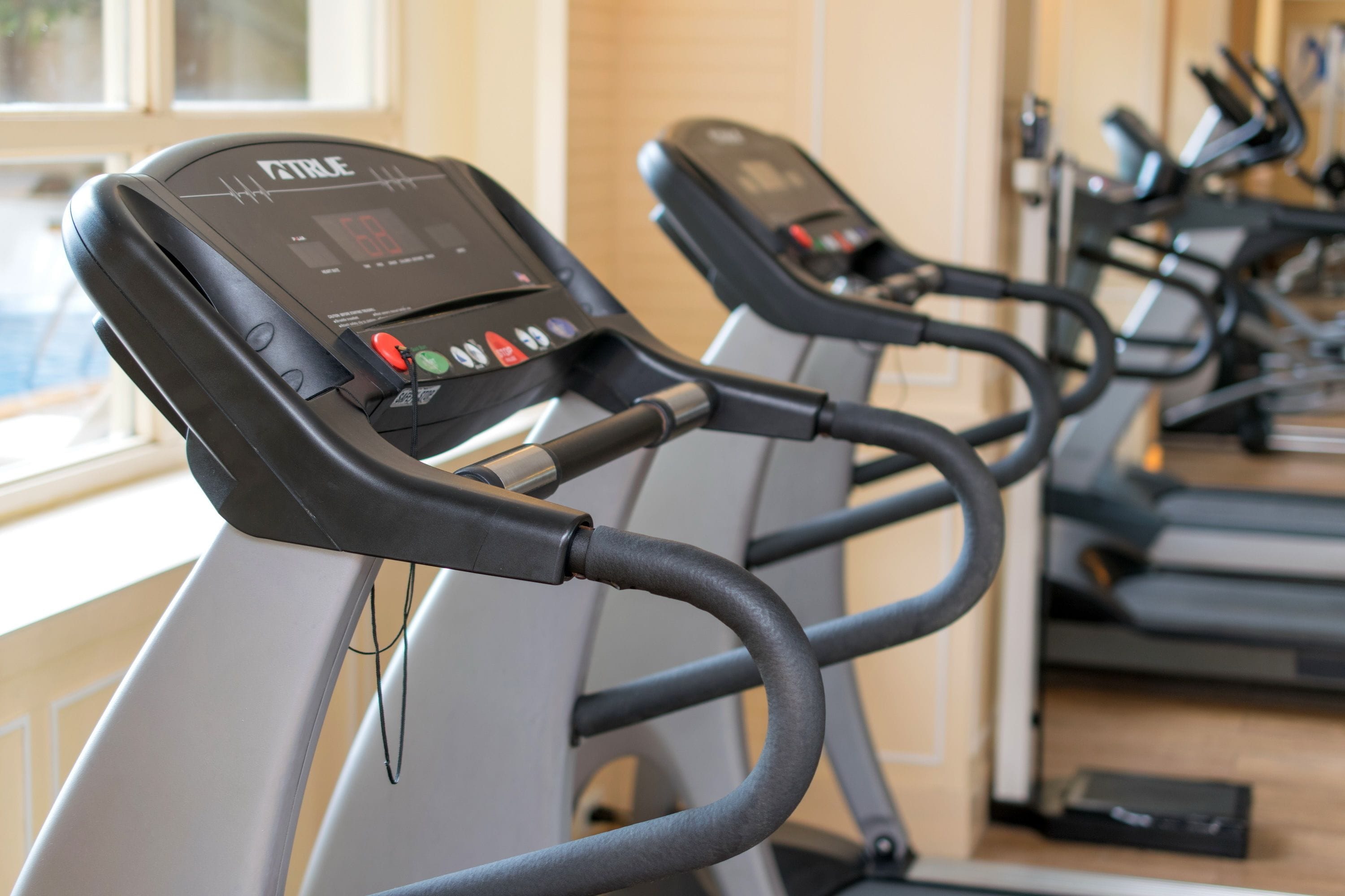 Varias cintas de correr en un gimnasio, con pantallas digitales en la parte frontal.