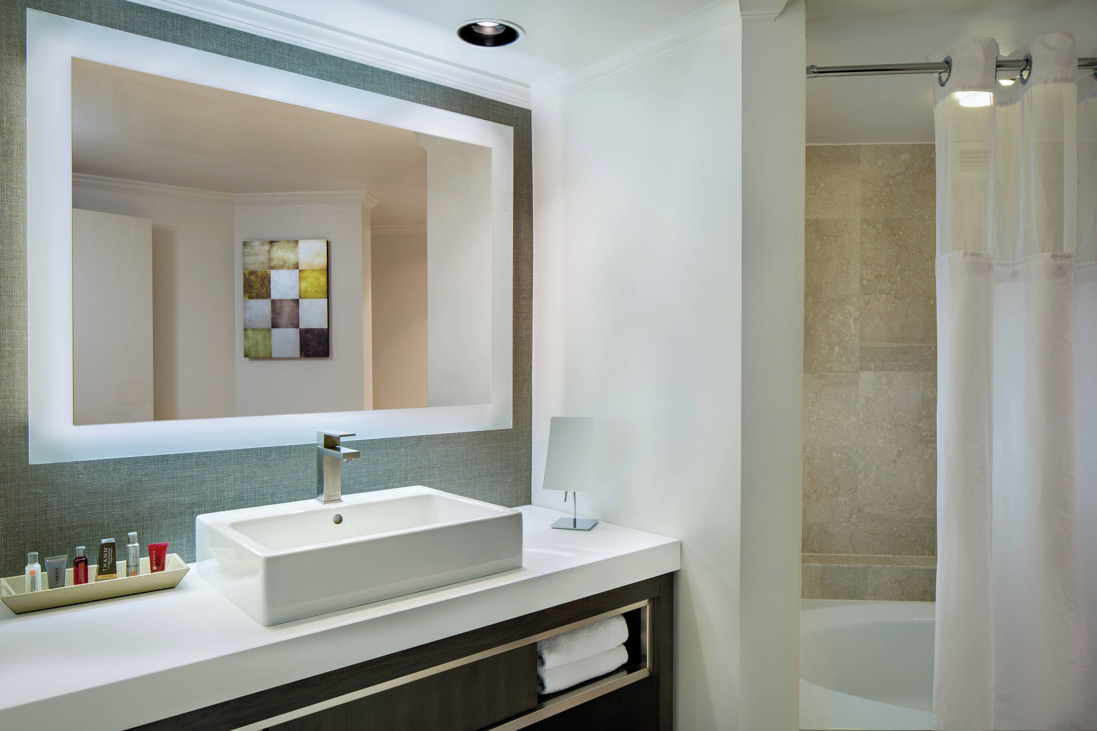 A modern bathroom with a large mirror, a white sink, a towel rack, and a shower curtain.
