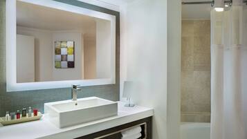 A modern bathroom with a large mirror, a white sink, a towel rack, and a shower curtain.