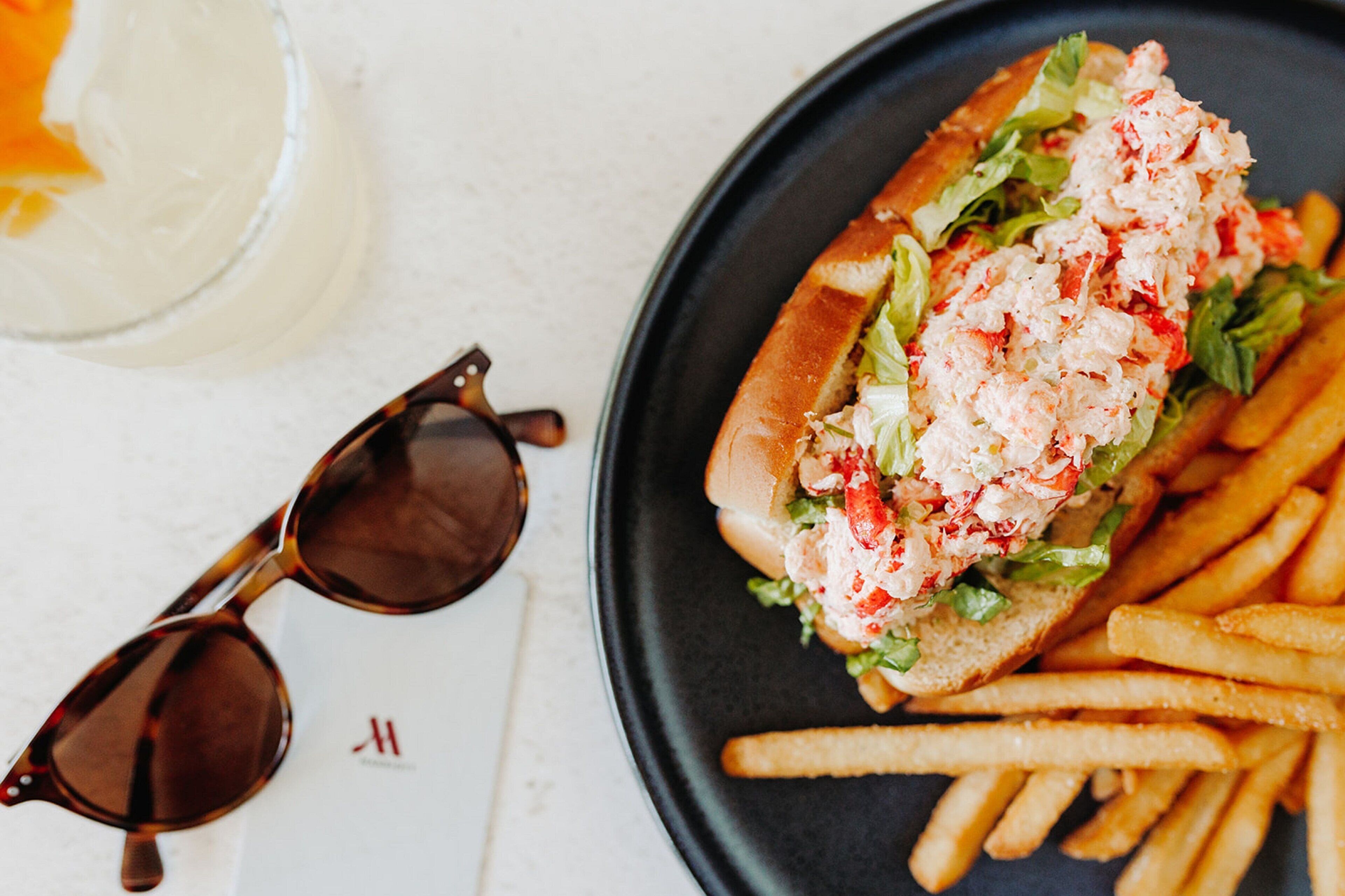 Un sandwich accompagné de frites, servi sur une assiette, avec des lunettes de soleil et une boisson.