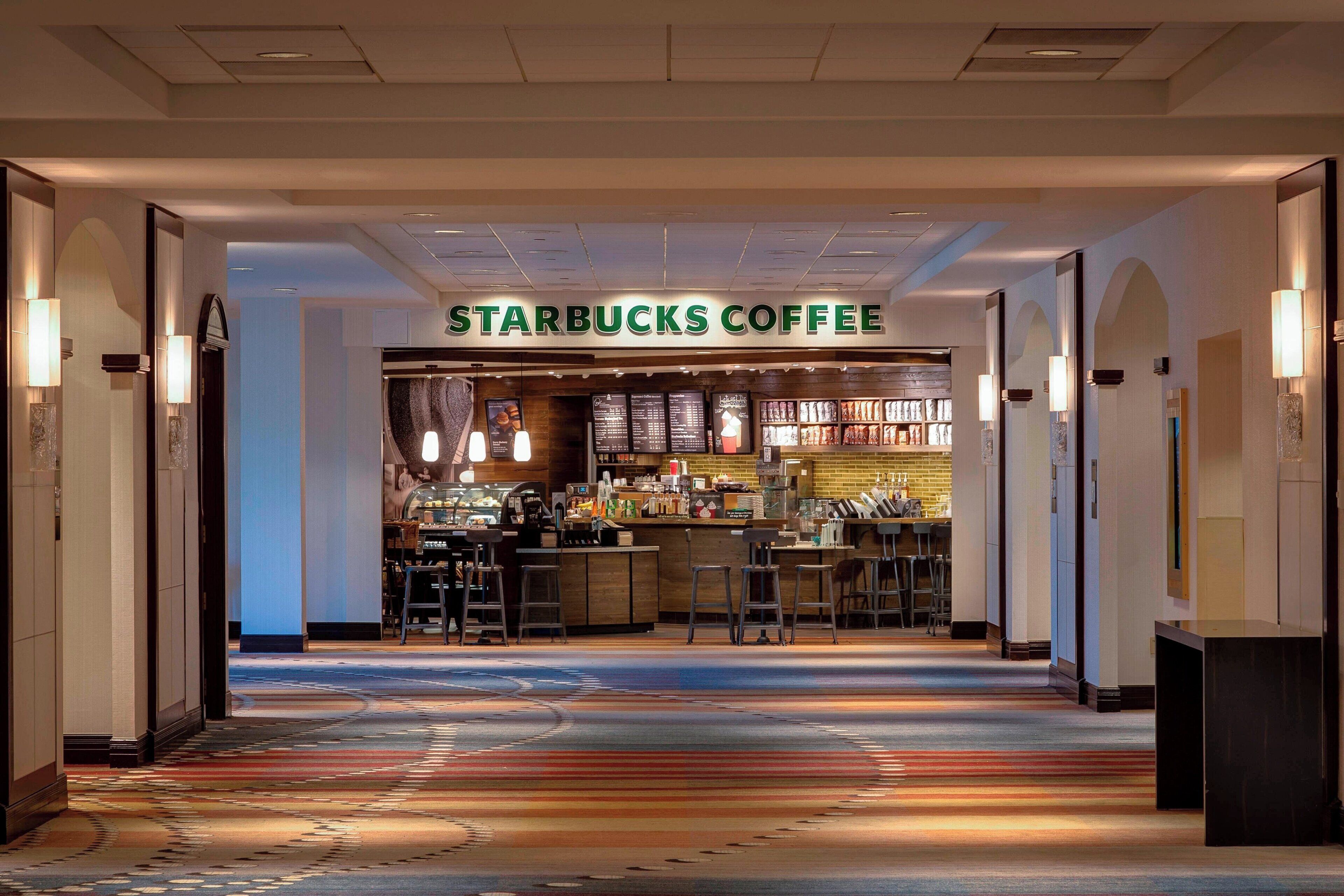 Una cafetería Starbucks en el vestíbulo de un hotel, con piso alfombrado y una zona de bar.