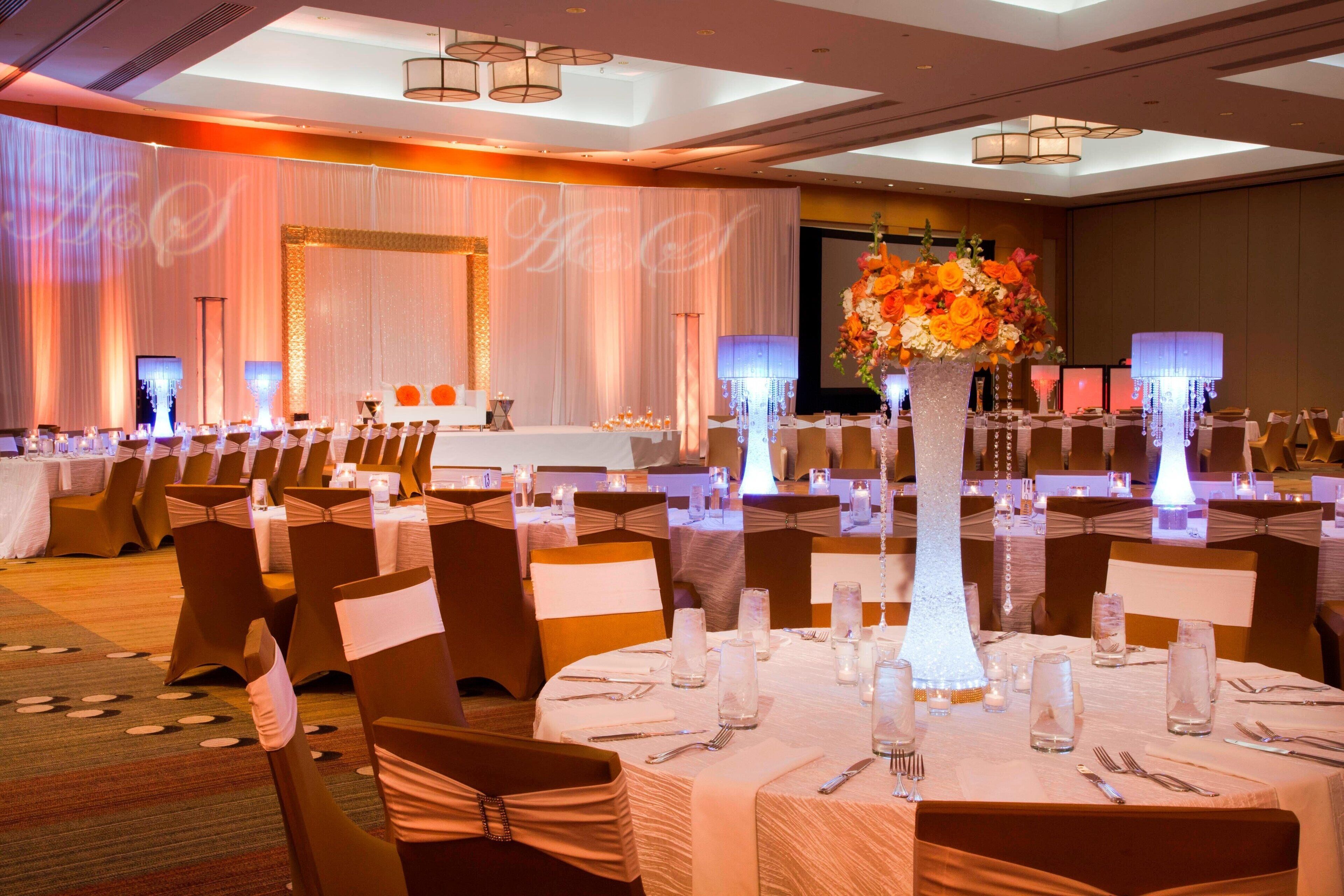 A banquet hall with round tables, chairs, and a large floral centerpiece.