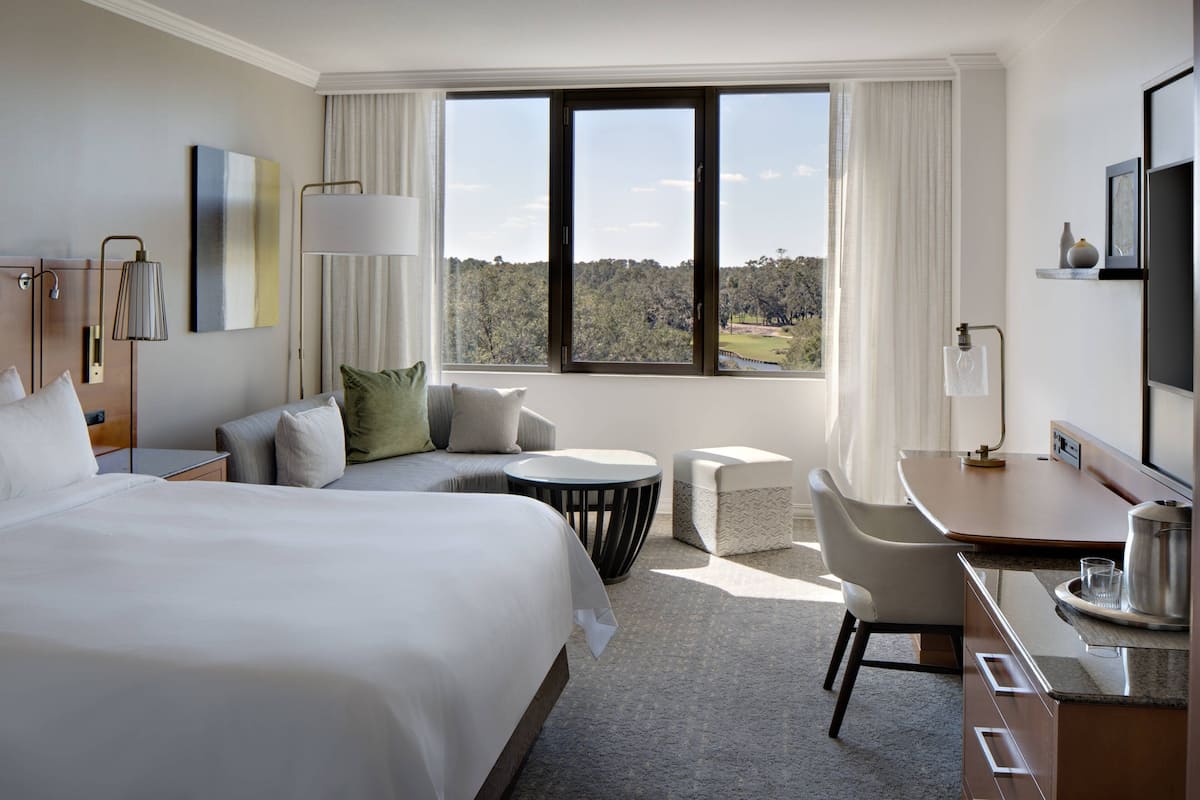 A hotel room with a large bed, a desk, a chair, and a view of the outdoors.