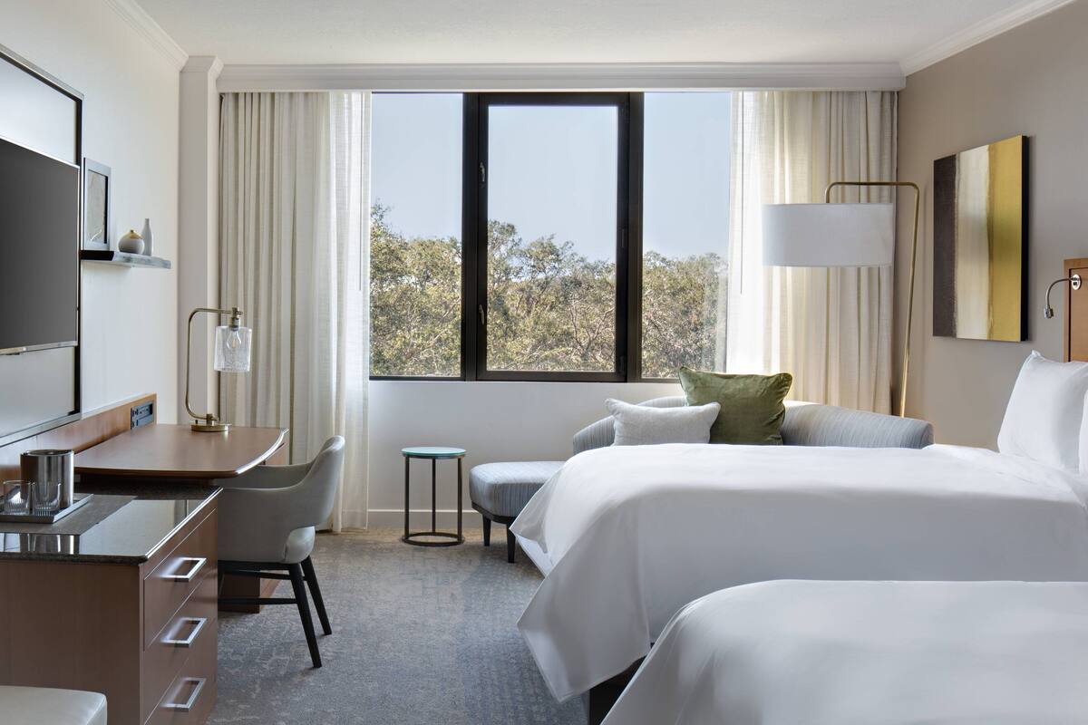A hotel room with a bed, a desk, a chair, a lamp, and a window with curtains.
