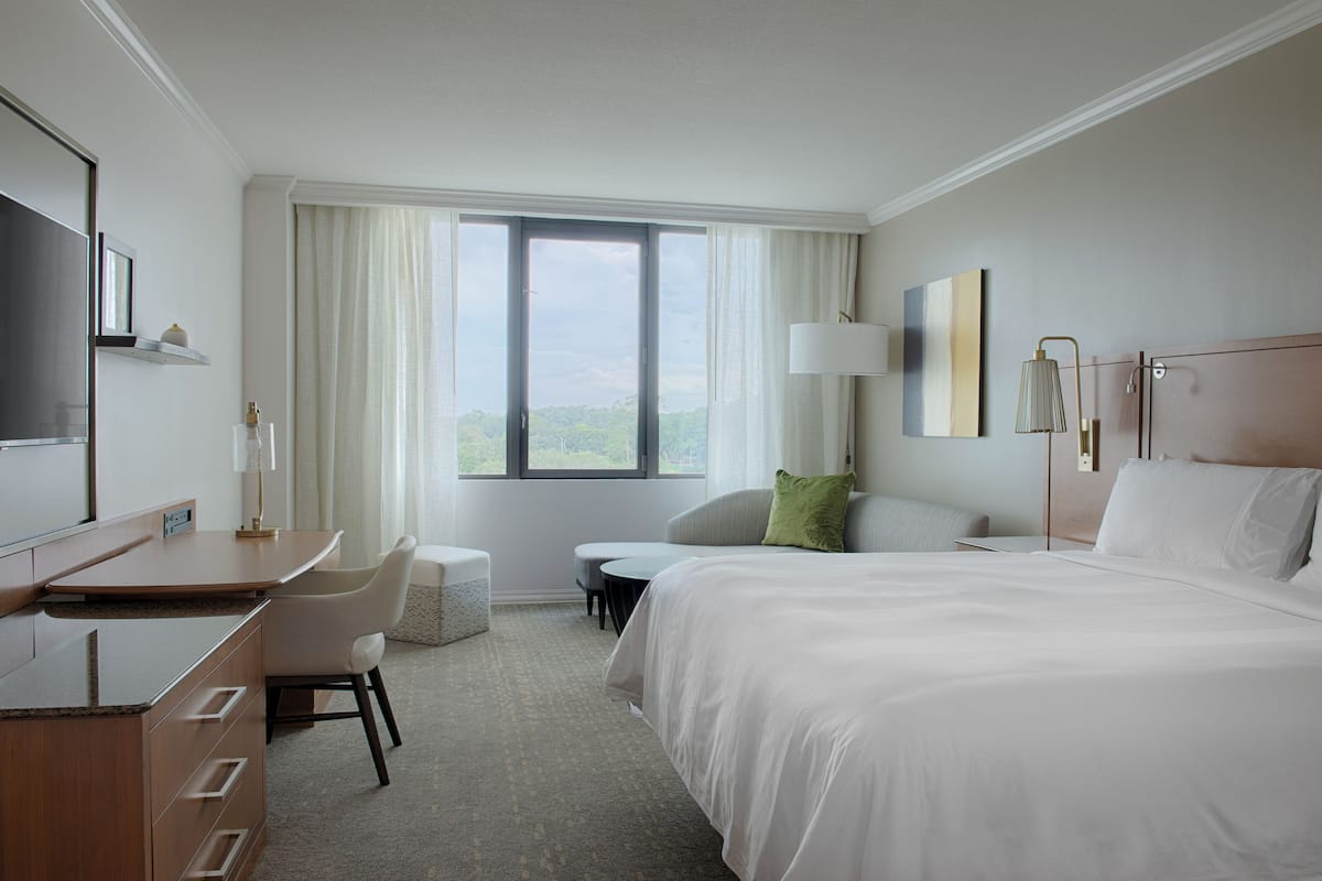 A hotel room with a bed, a desk, a chair, a small table, and a window with curtains.