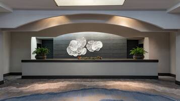 A reception area with a modern design, featuring a large, curved reception desk, two potted plants, and a decorative wall piece.