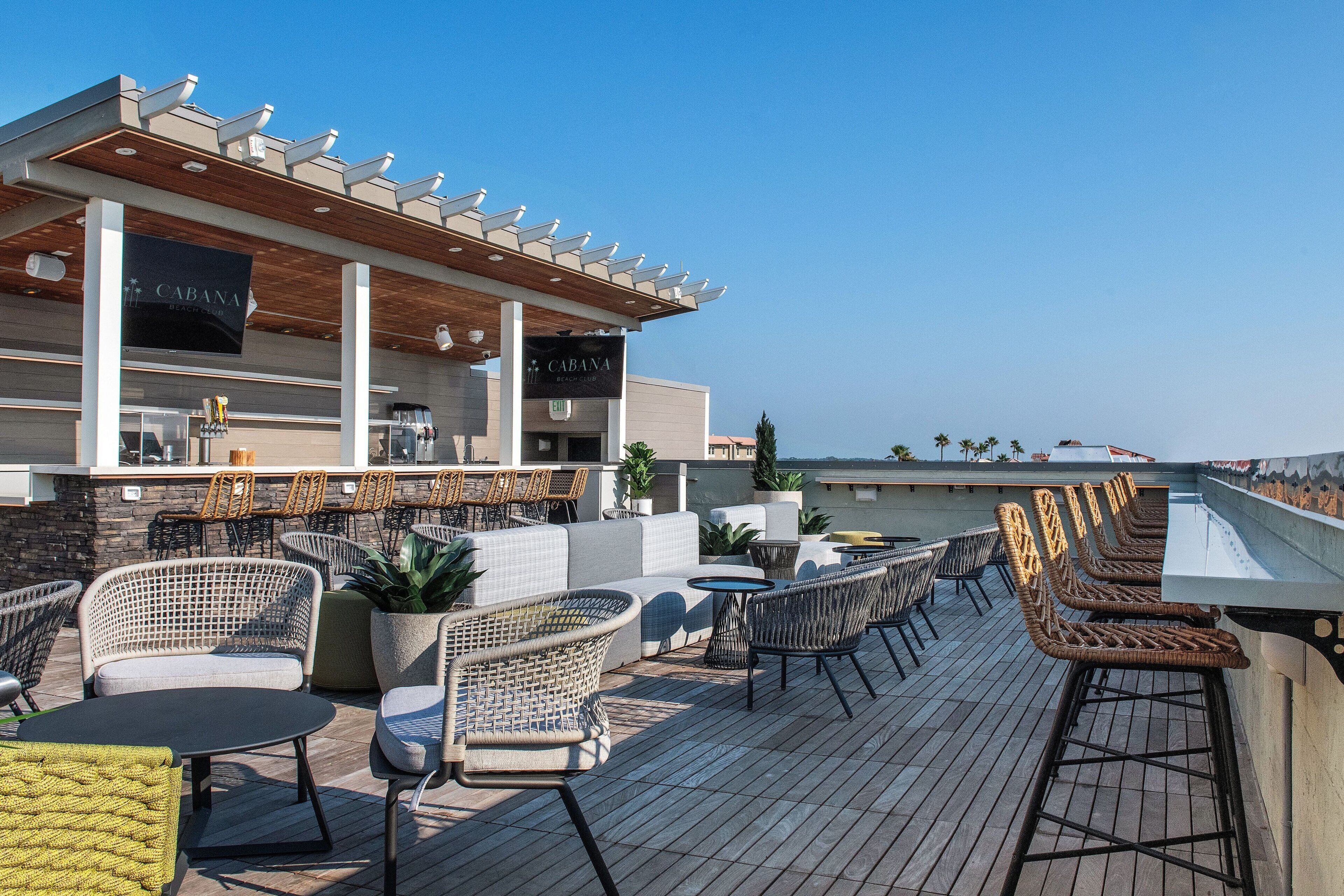 A rooftop bar with wicker furniture, a wooden pergola, and a view of the ocean.