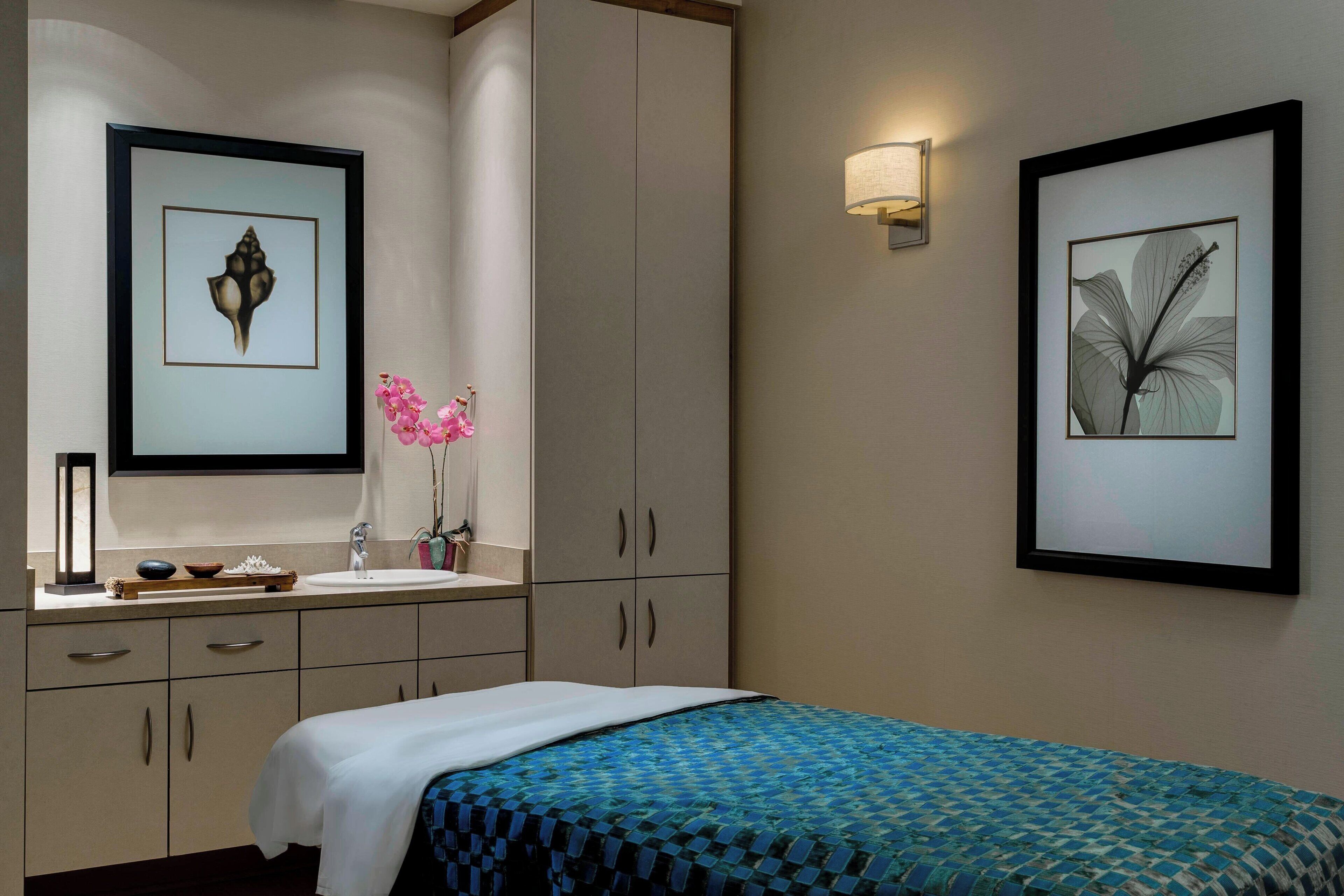 A hotel room with a bed, a sink, and cabinets. There are framed pictures on the wall and a vase with flowers on the counter.