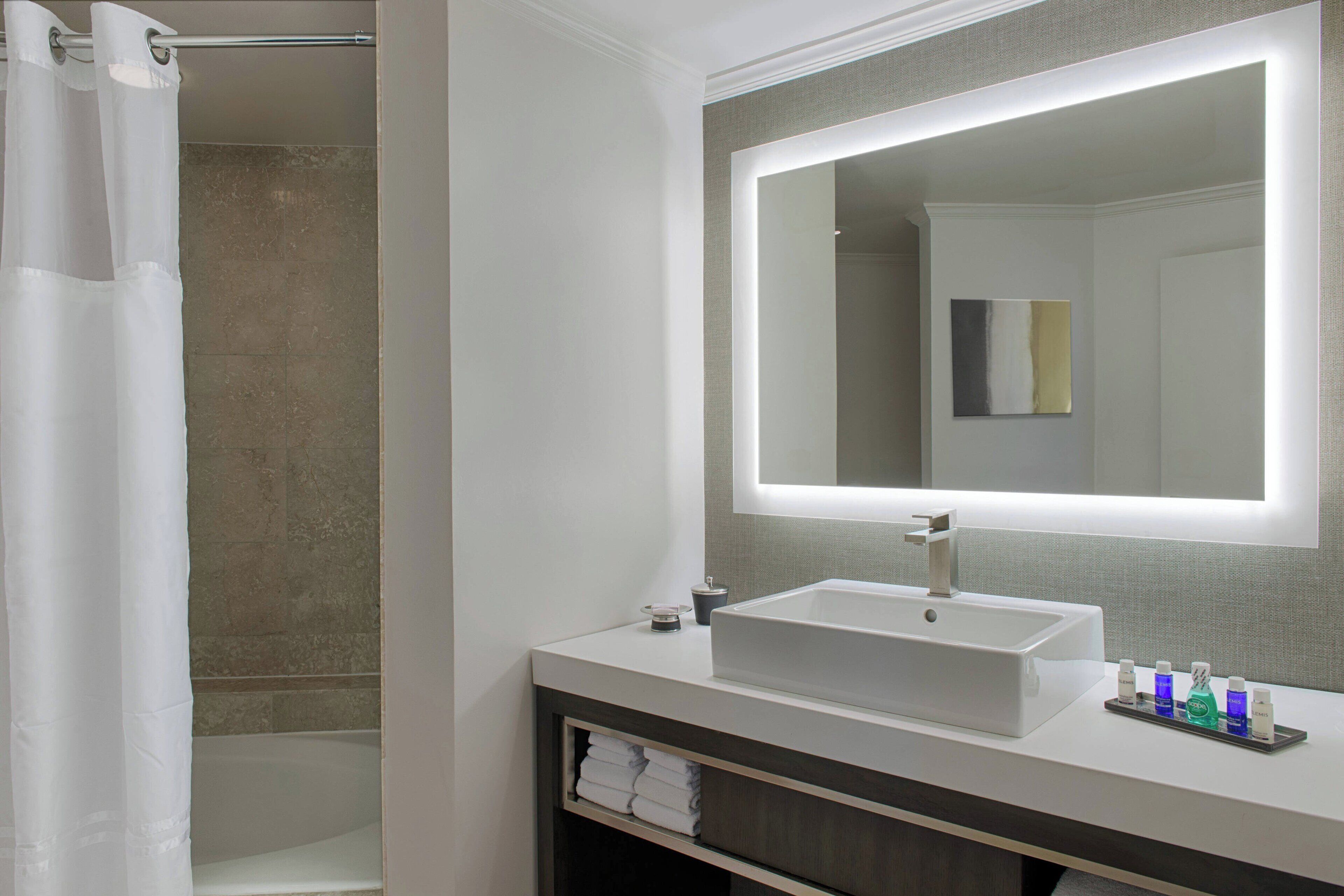 Un baño moderno con un lavabo blanco, un espejo con iluminación integrada y una cortina de ducha.