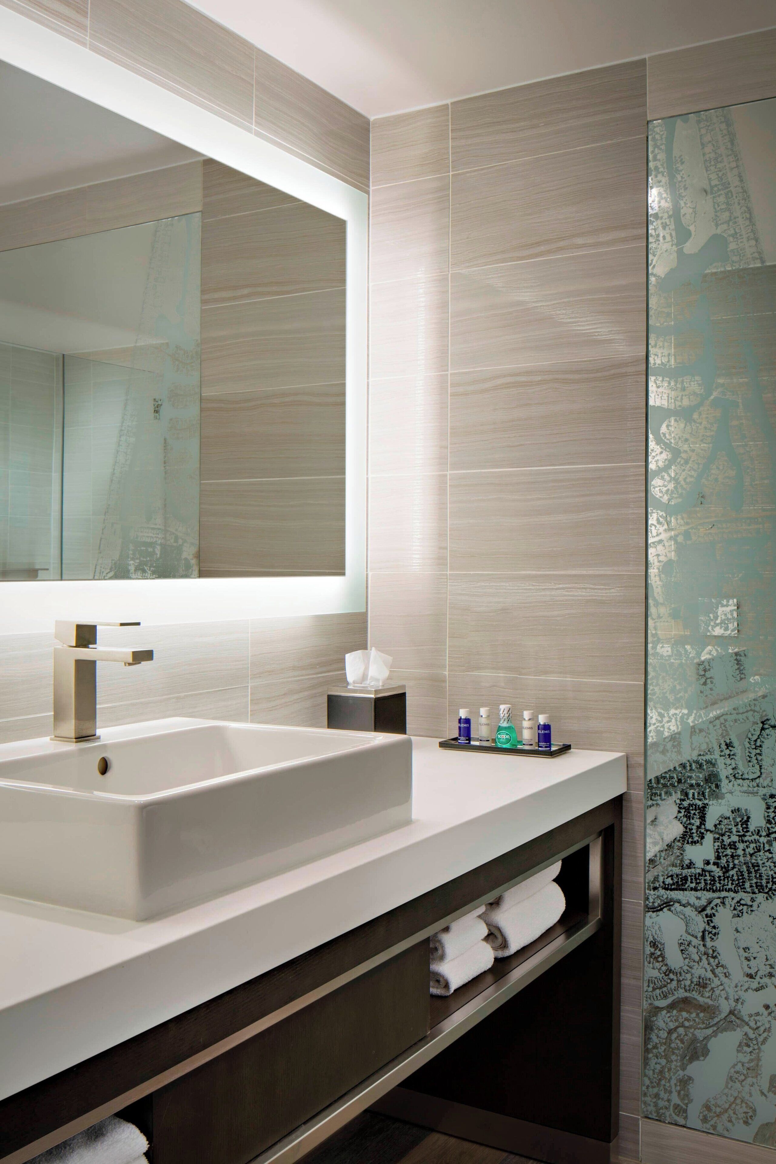 Une salle de bain moderne avec un grand miroir, un lavabo blanc et une cabine de douche en verre.