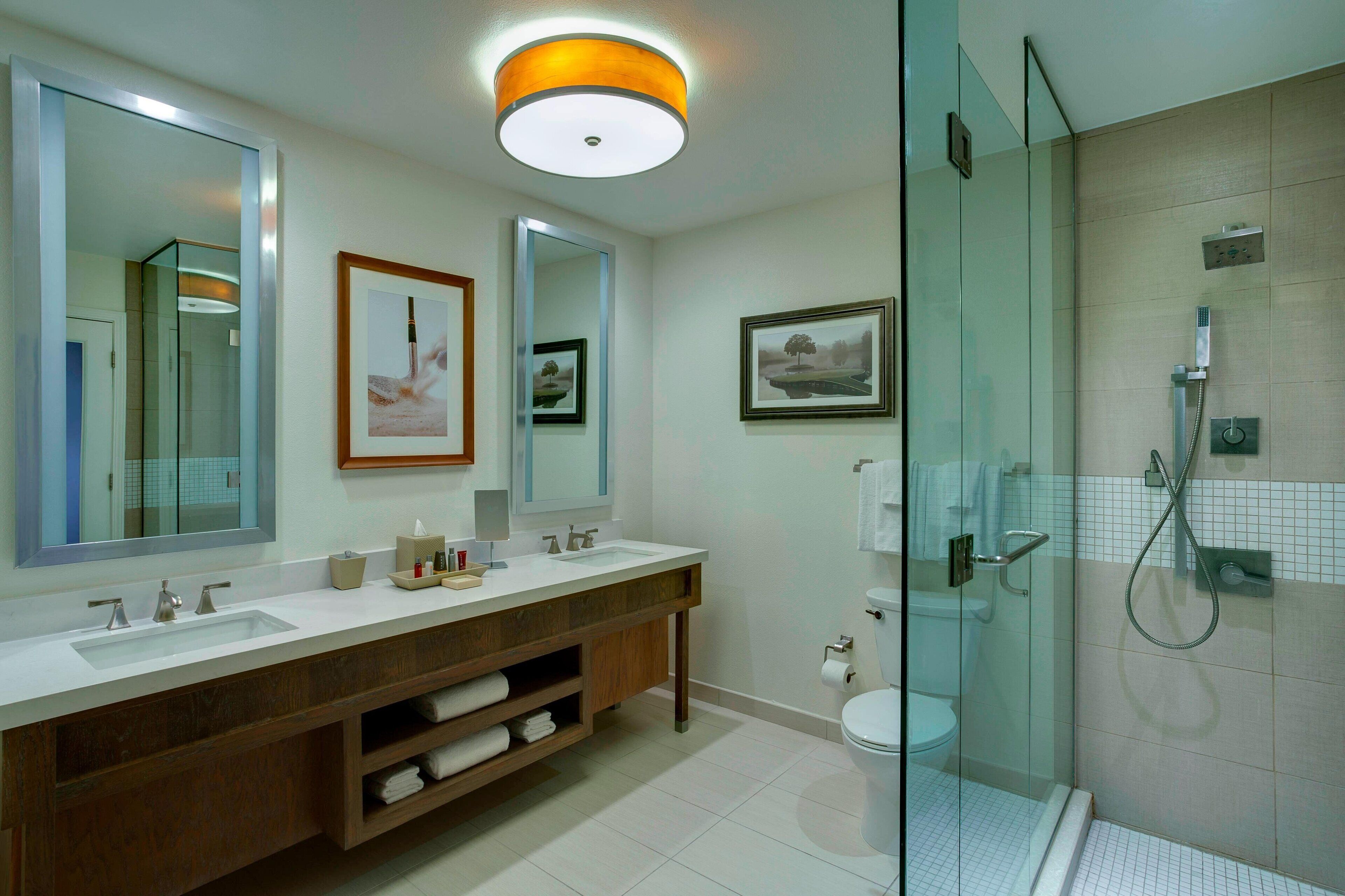 A modern bathroom with a glass-enclosed shower, a double sink vanity, and large mirrors.