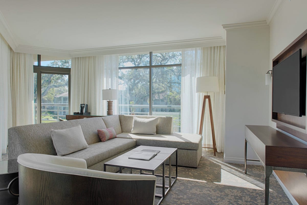 A modern living room with a sectional sofa, a coffee table, a TV, and large windows with curtains.
