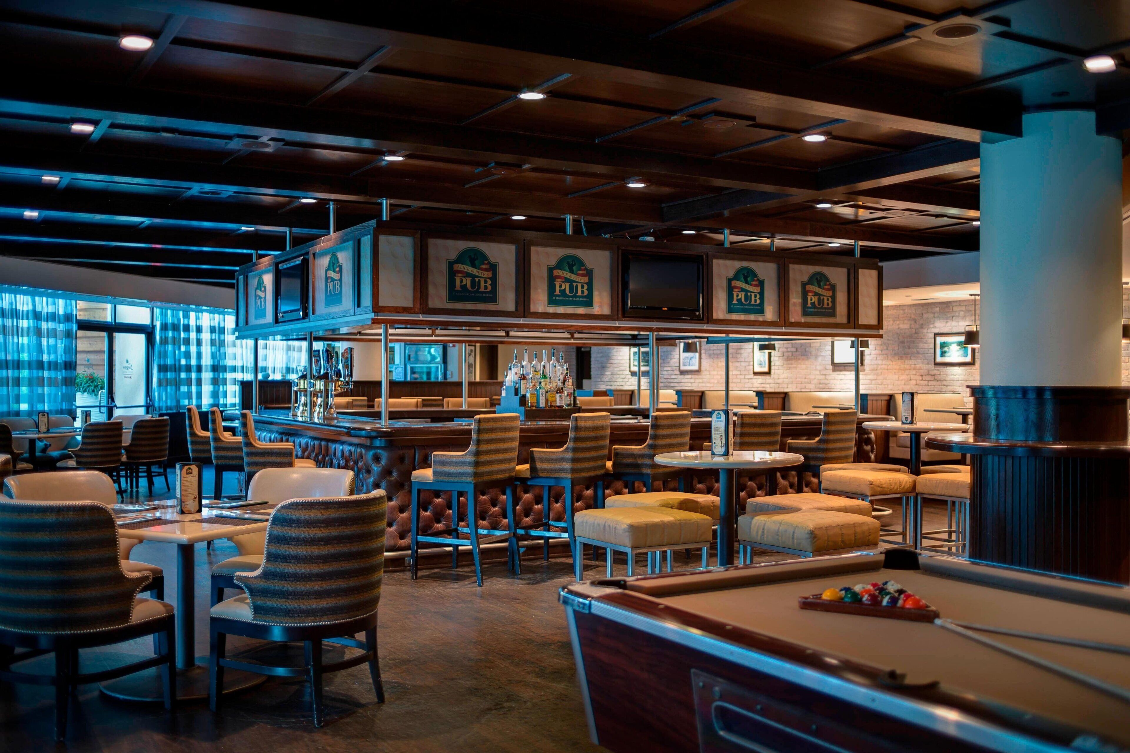 A bar area with multiple seating options, including bar stools and tables, and a pool table.