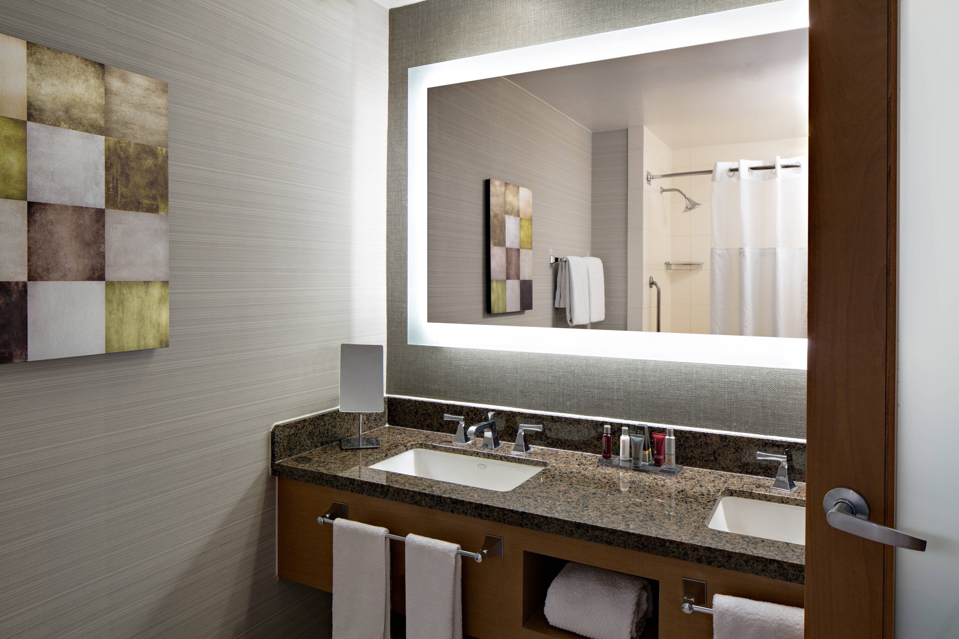 A modern bathroom with two sinks, a large mirror, and a shower visible in the reflection.