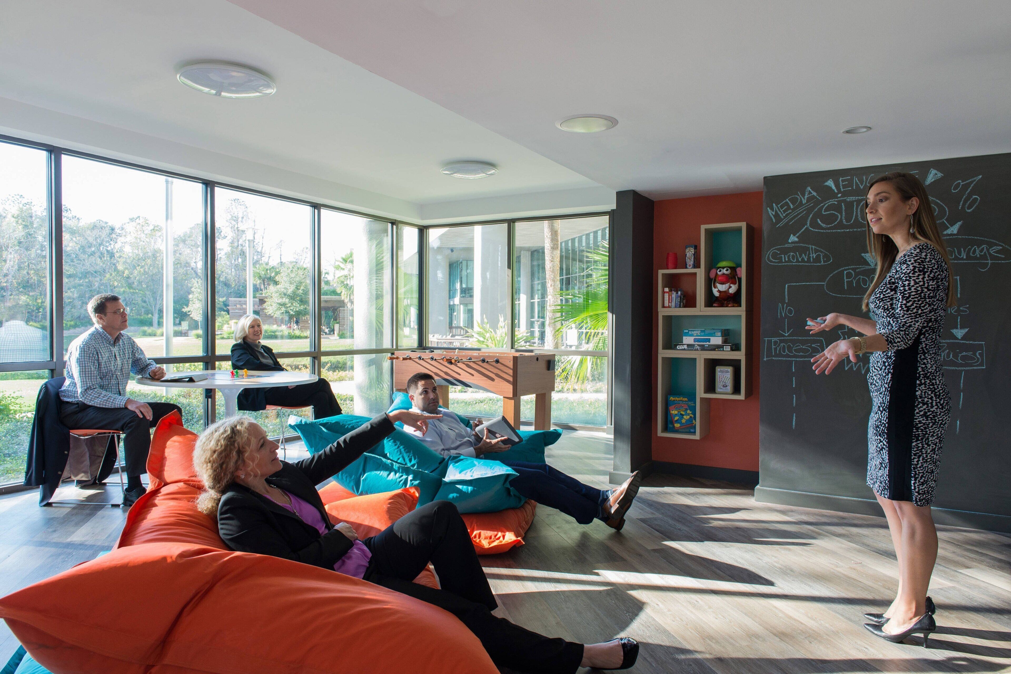 A modern meeting room with large windows, comfortable seating, and a presentation area with a blackboard.