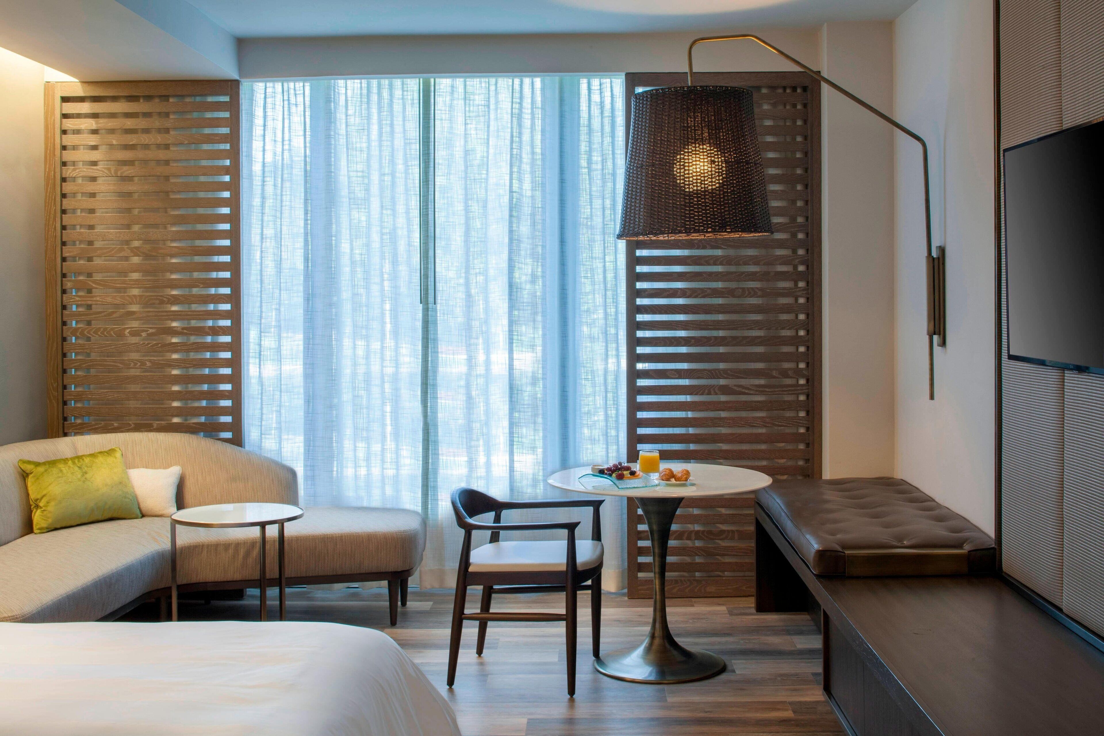 A modern hotel room with a bed, a sofa, a dining table with breakfast, and a TV.