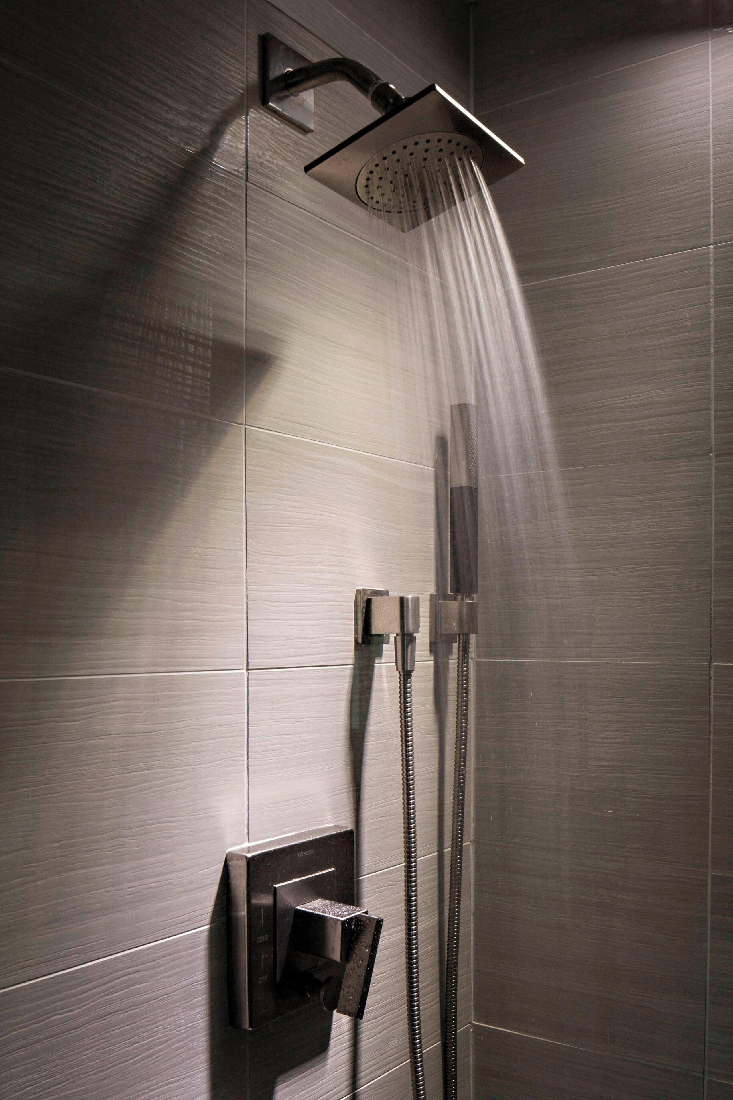 A modern shower with a handheld showerhead and a fixed overhead showerhead, both mounted on a metallic wall.