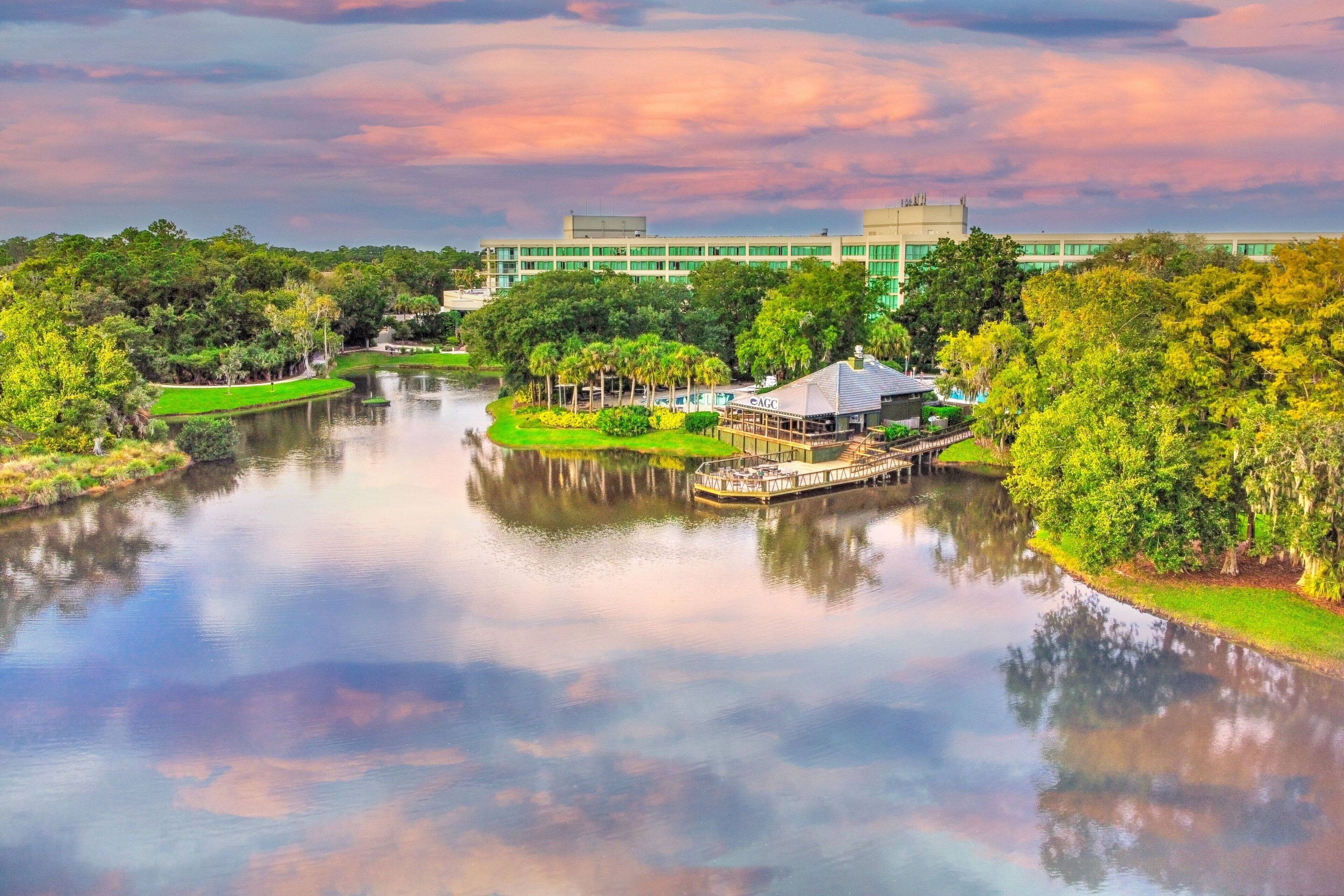 A serene riverside view with a gazebo, lush greenery, and a modern building in the background.