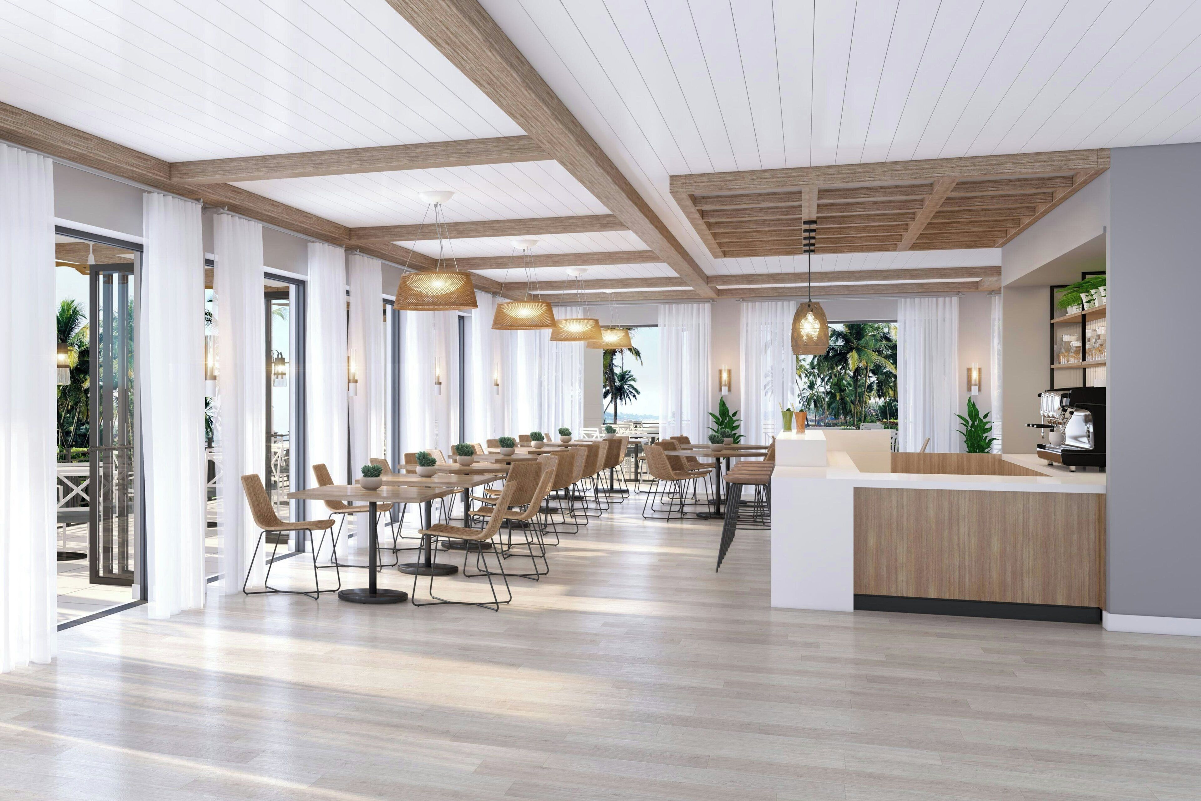 A spacious dining area with wooden tables and chairs, pendant lighting, and a kitchen counter.