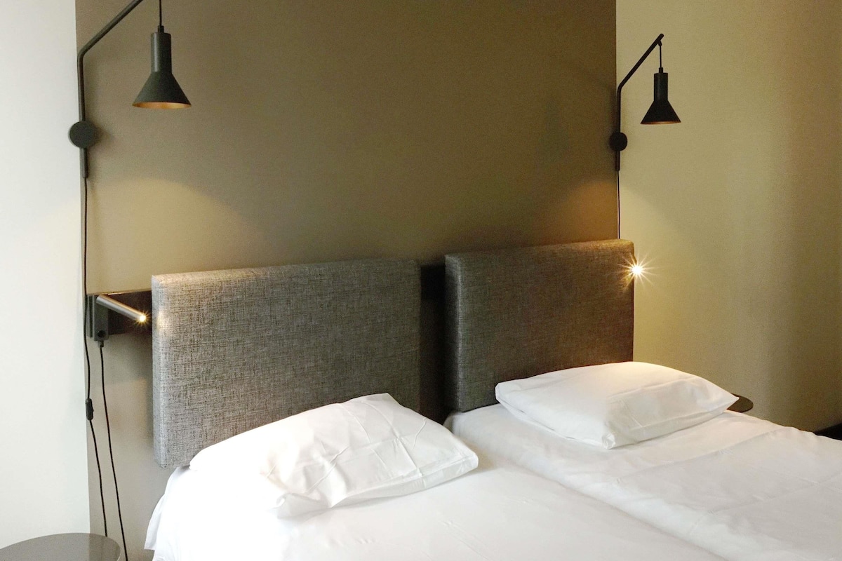 A hotel room with a bed, two bedside lamps, and a headboard.