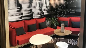 Espaço de convívio com um sofá vermelho, uma mesa redonda branca e uma obra de arte na parede com tema de xadrez.