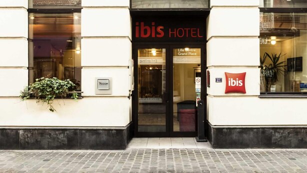 Exterior do hotel ibis com entrada clara, placa indicando localização como Lille Centre Grand Place e logotipo ACCOR visível.
