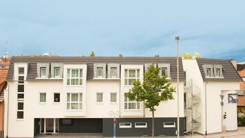 Ein modernes, mehrgeschossiges Wohngebäude mit flachem Dach, zahlreichen Fenstern und einem sichtbaren Garageneingang.