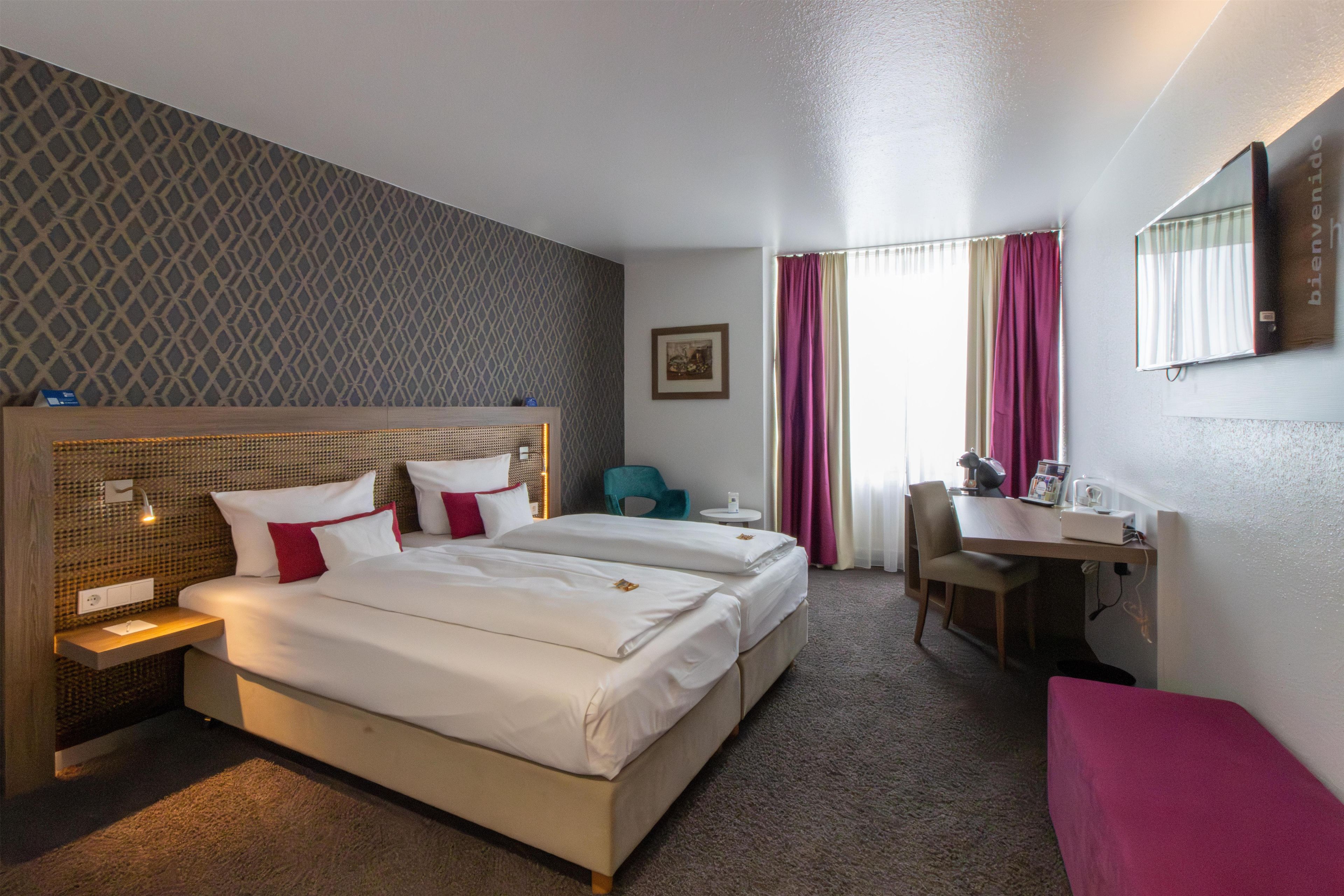 A hotel room with two beds, a desk, a chair, and a small table.