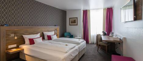 A hotel room with two beds, a desk, a chair, and a small table.