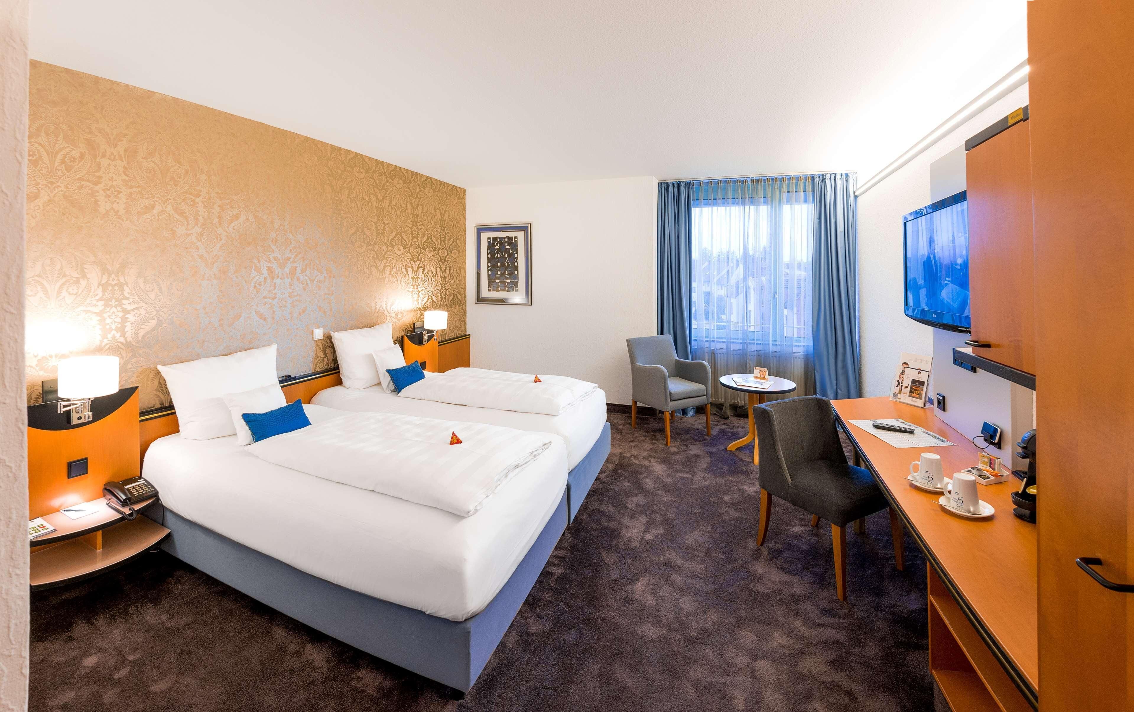 A hotel room with two beds, a desk with a chair, a TV, and a small table with a chair.