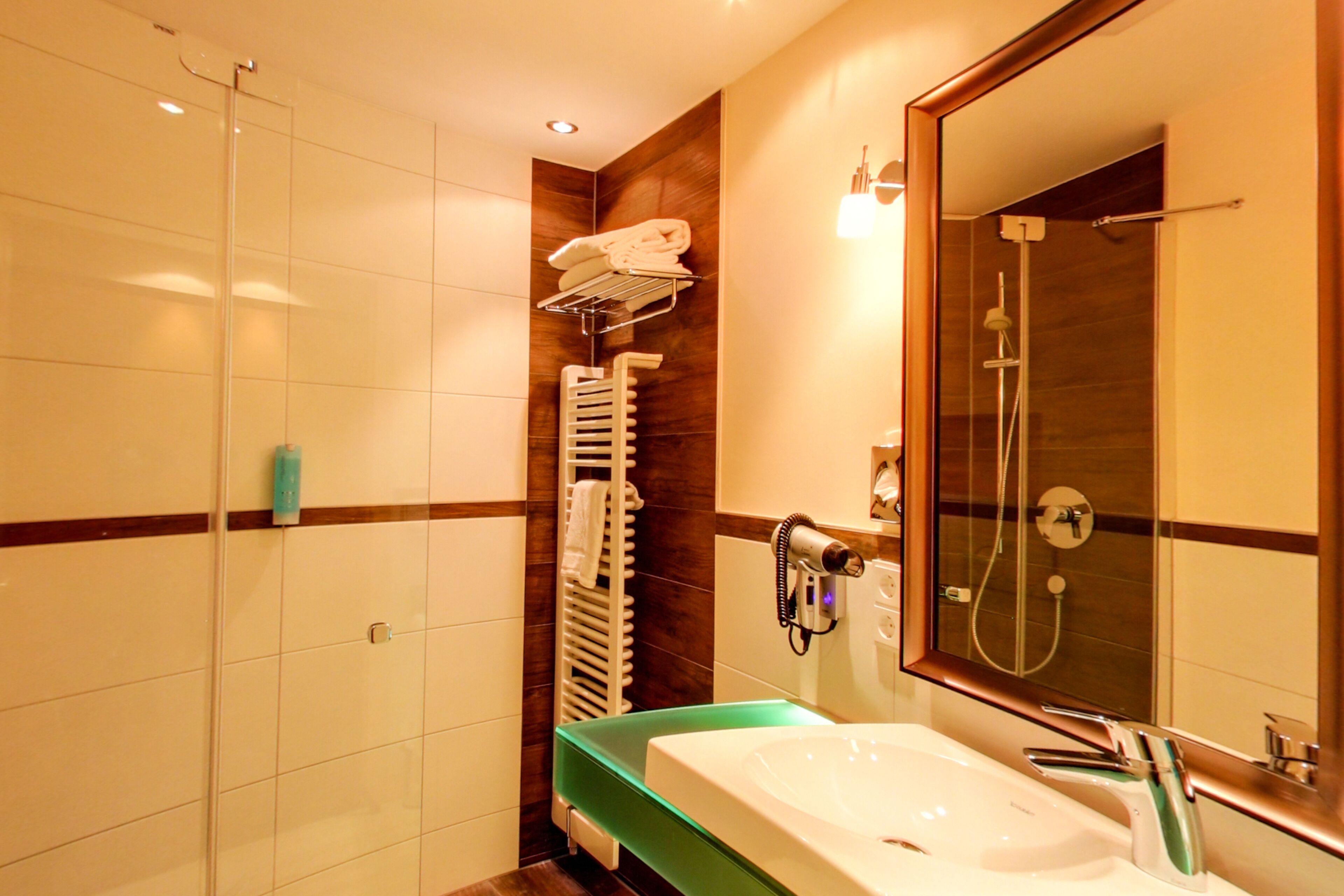 A modern bathroom with a glass shower enclosure, a built-in sink with a green countertop, and a large mirror above the sink.