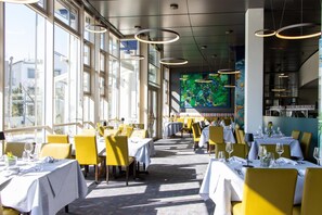 A restaurant with yellow chairs and tables, large windows, and a mural on the wall. - Best Western Plus Palatin Kongresshotel (Wiesloch)