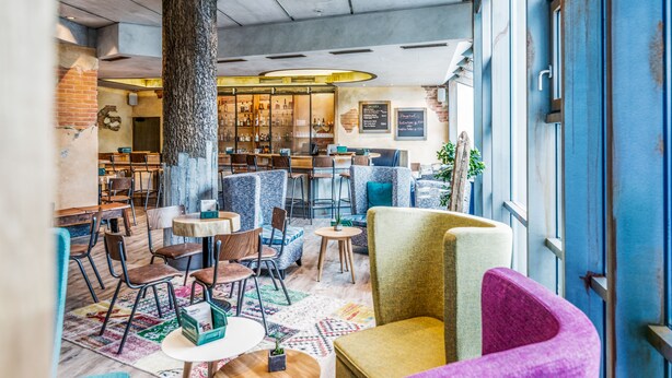 Ein gemütliches Café mit Holztischen und -stühlen, einem großen Baumstamm als Mittelpunkt und einer Bar im Hintergrund.