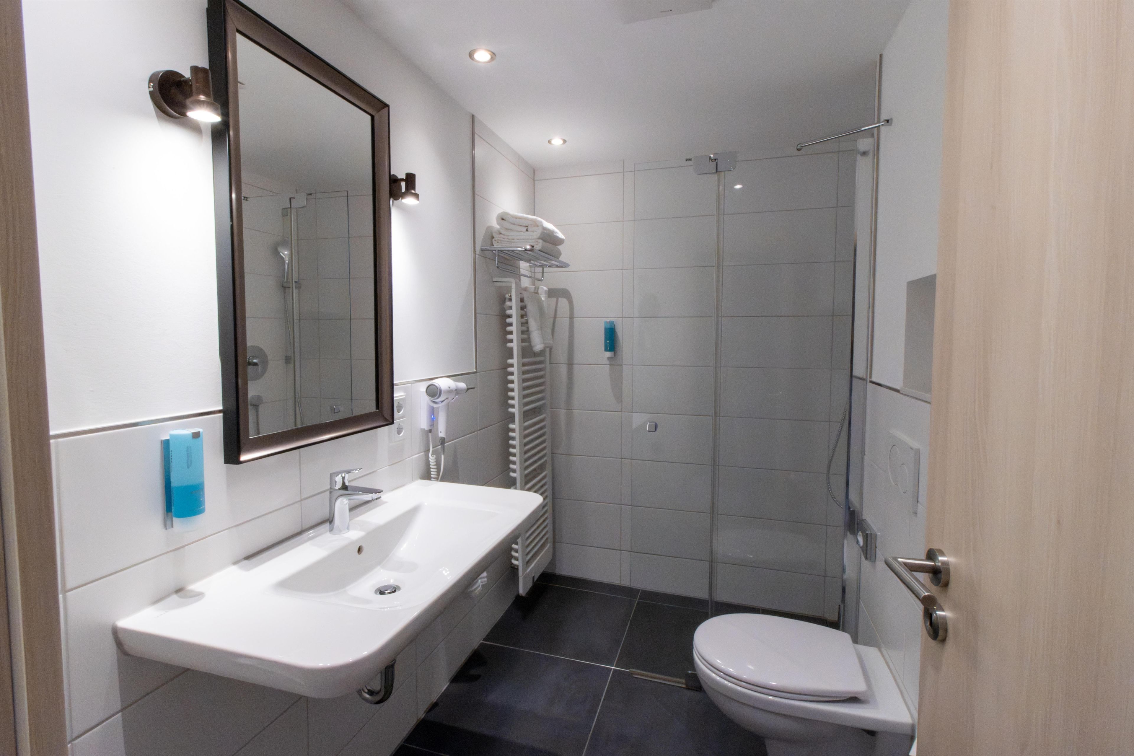 A modern bathroom with a sink, mirror, toilet, and shower.