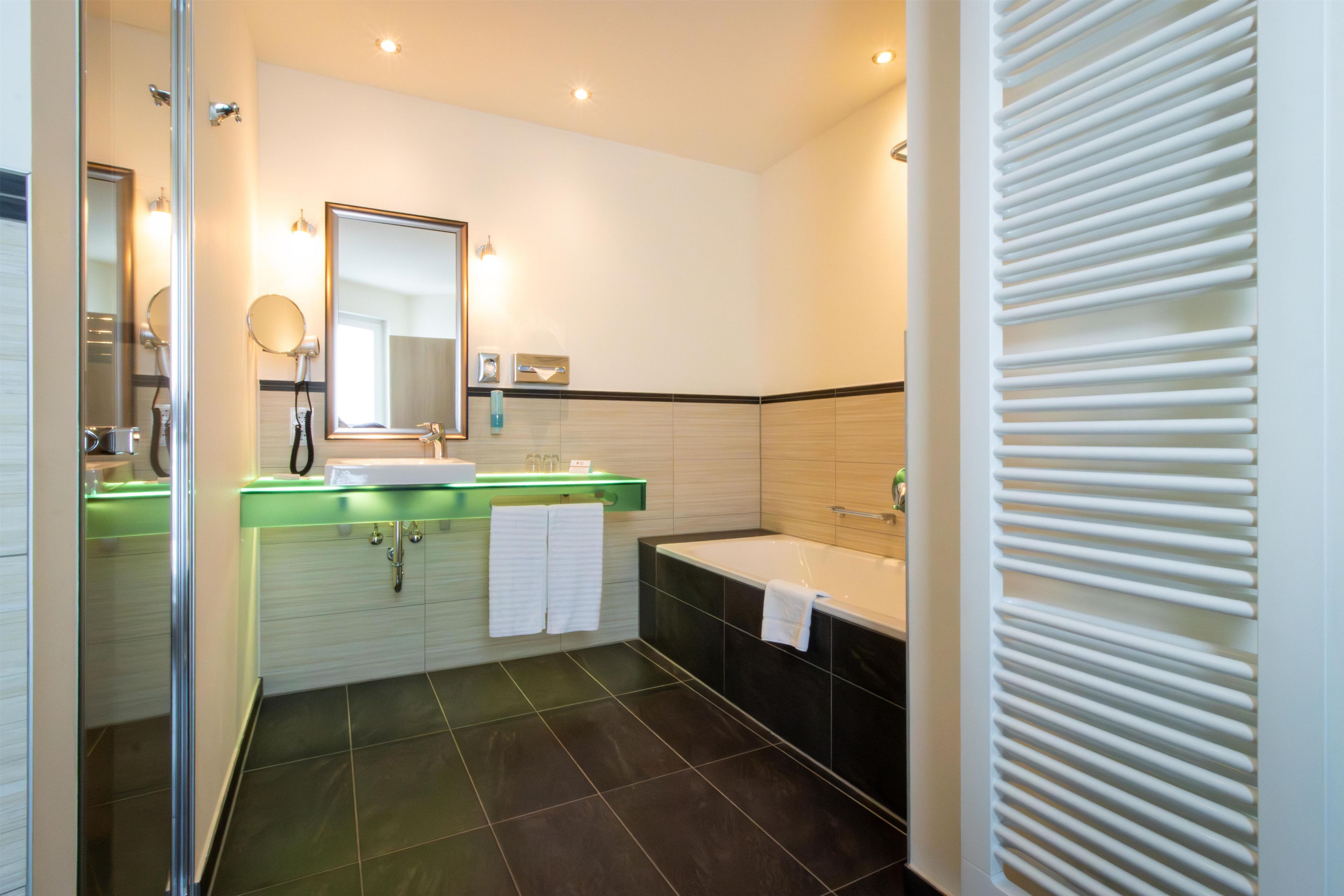 A modern bathroom with a glass shower enclosure, a vanity with a green countertop, a large mirror, a bathtub, and a towel rack.