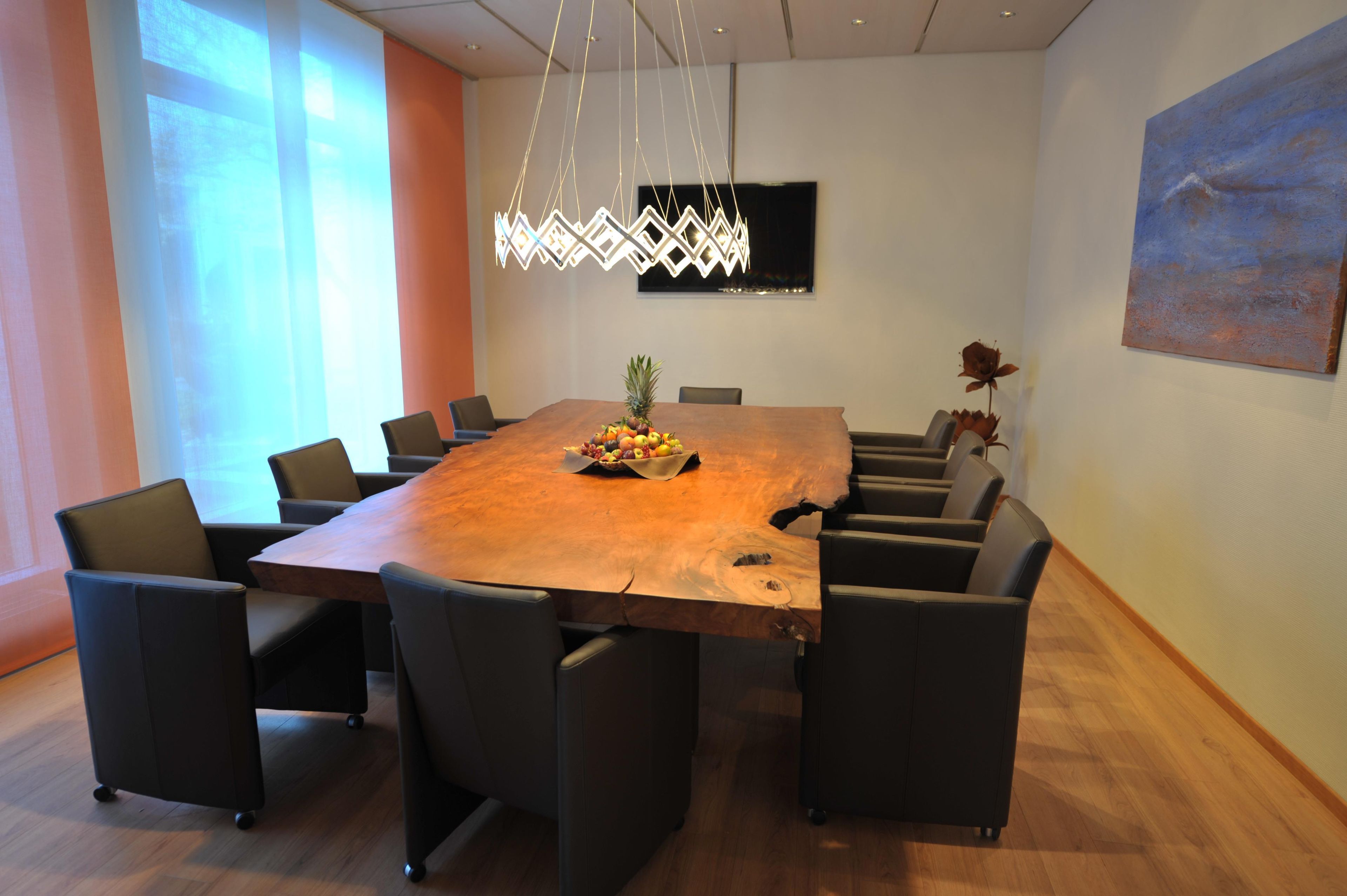 A conference room with a large wooden table, black chairs, a fruit centerpiece, and a modern chandelier.