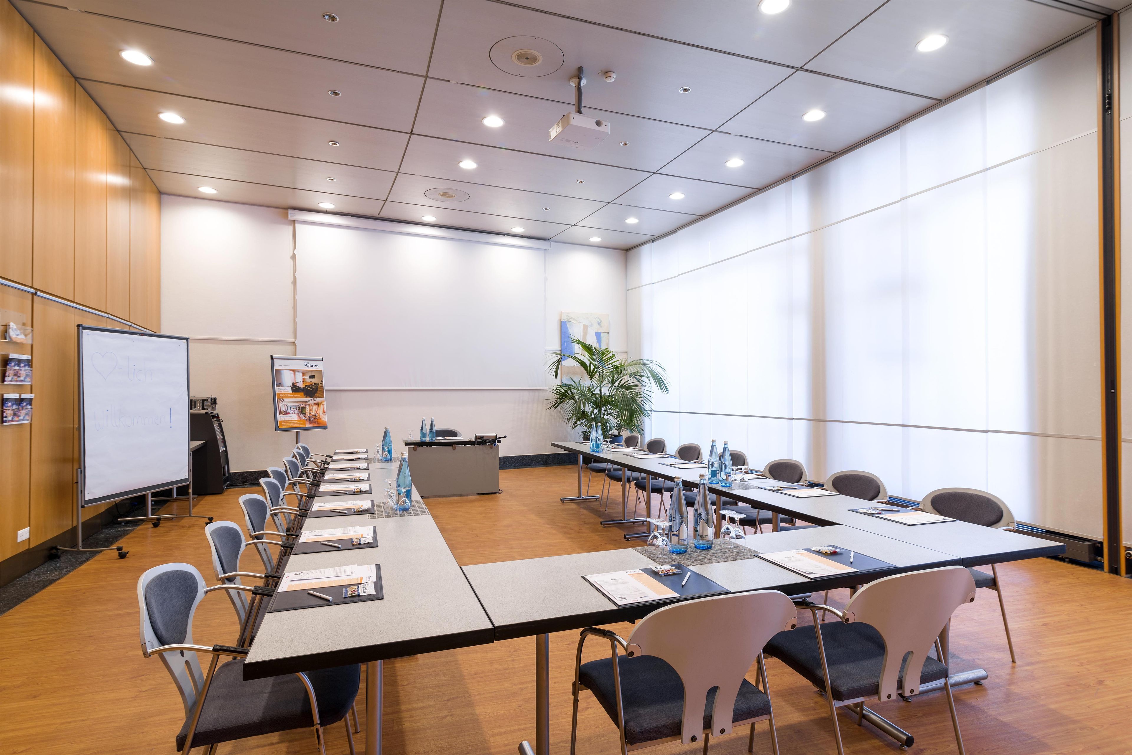 A conference room with a long table, chairs, a whiteboard, and a plant.