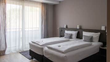 A hotel room with two beds, a large window with sheer curtains, a nightstand with a lamp, and a small table with a phone.
