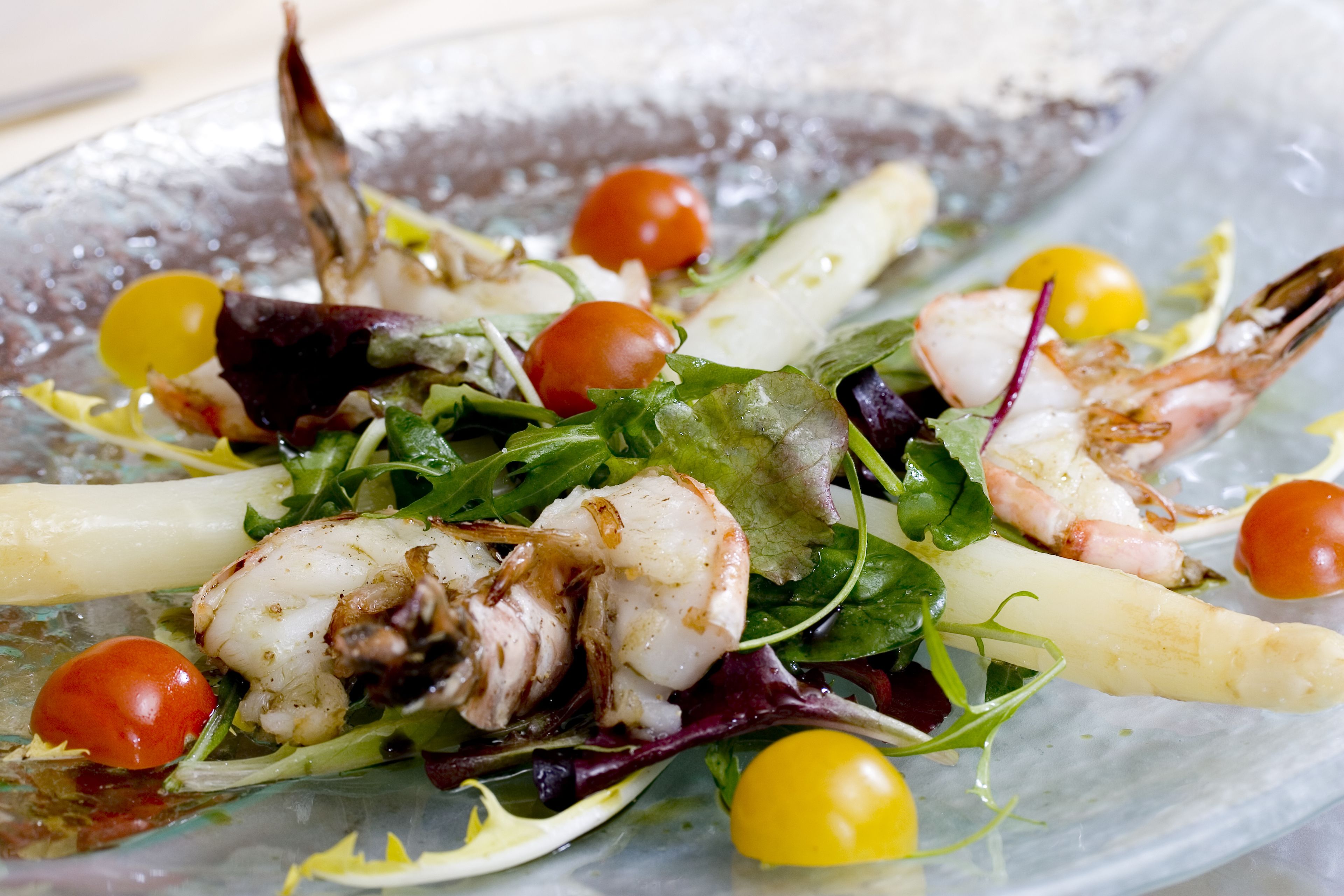 A seafood salad with shrimp, cherry tomatoes, and greens on a glass plate.