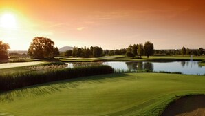 Un parcours de golf avec un étang, des arbres et un coucher de soleil.