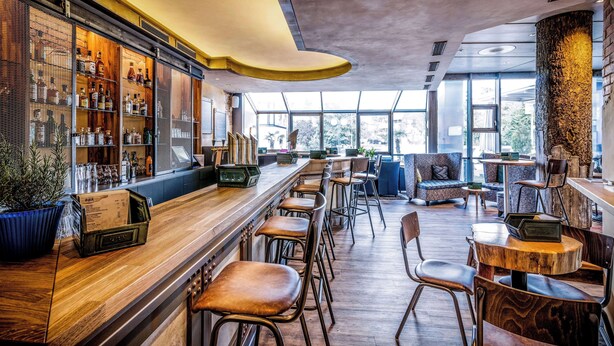 Eine Bar mit Holzböden, Hockstühlen und einer Sitzecke mit einer Couch und Sesseln.