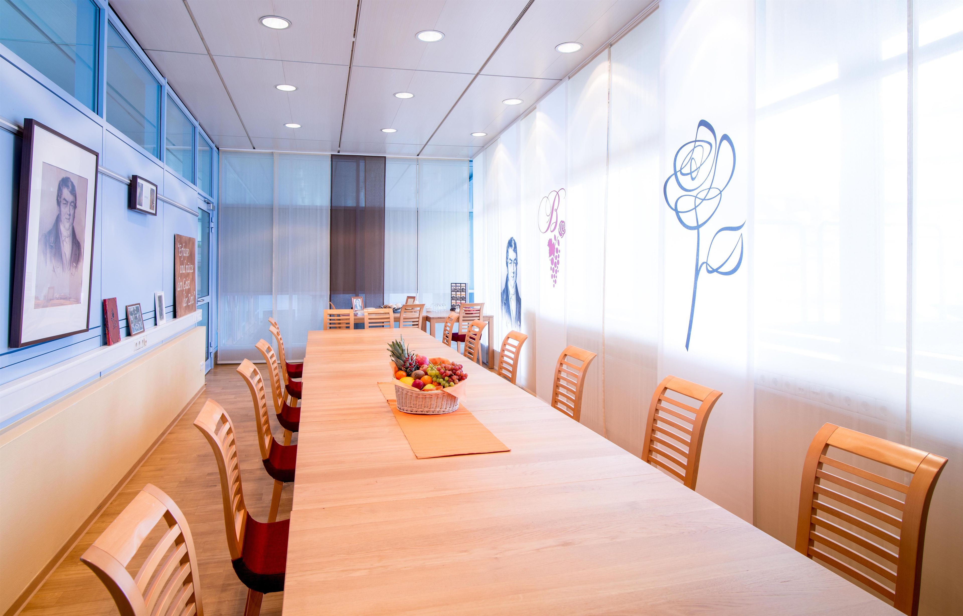 A conference room with a long table, chairs, framed pictures on the wall, and a fruit basket on the table.