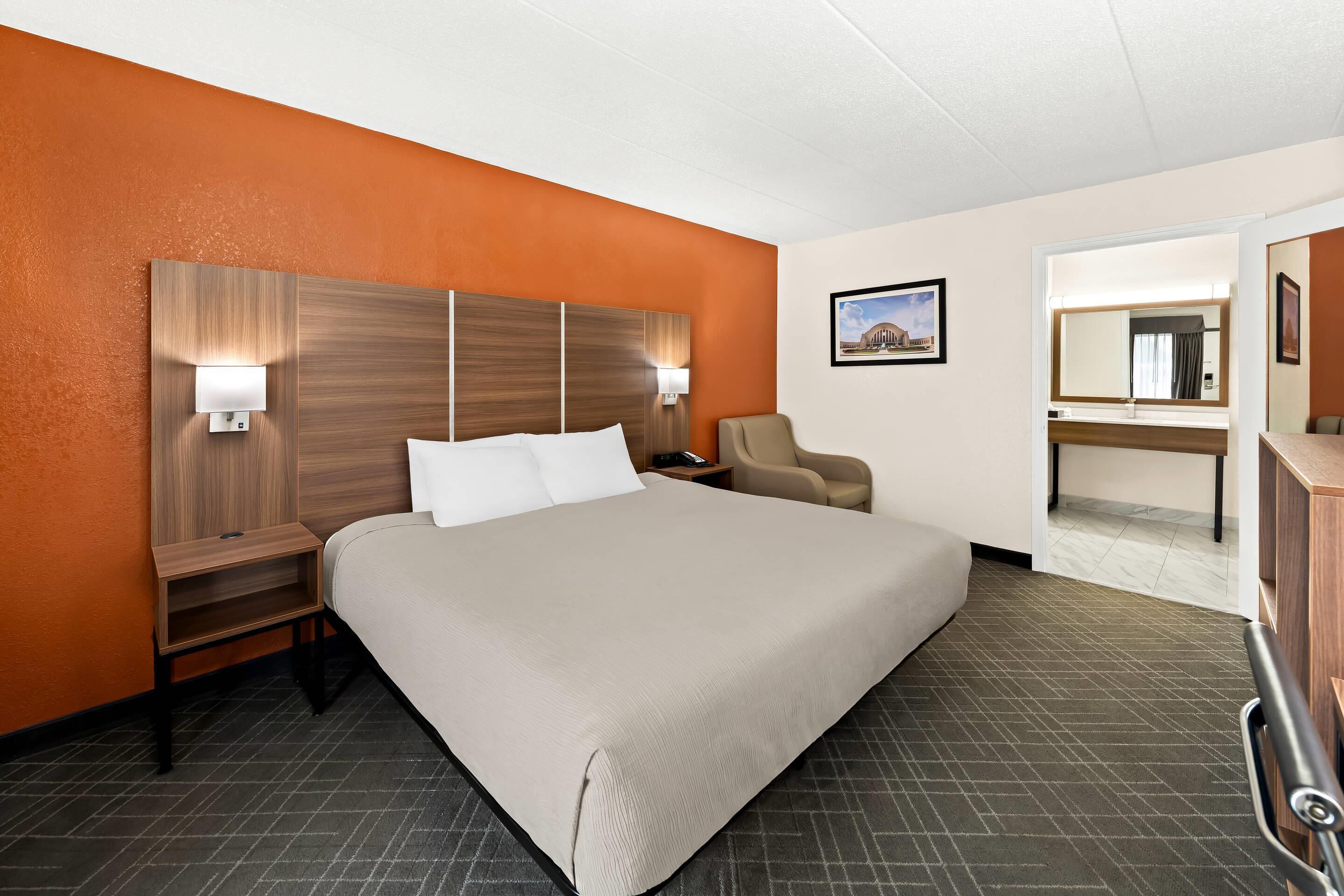 A hotel room with a large bed, a nightstand, a chair, a desk, and a mirror.