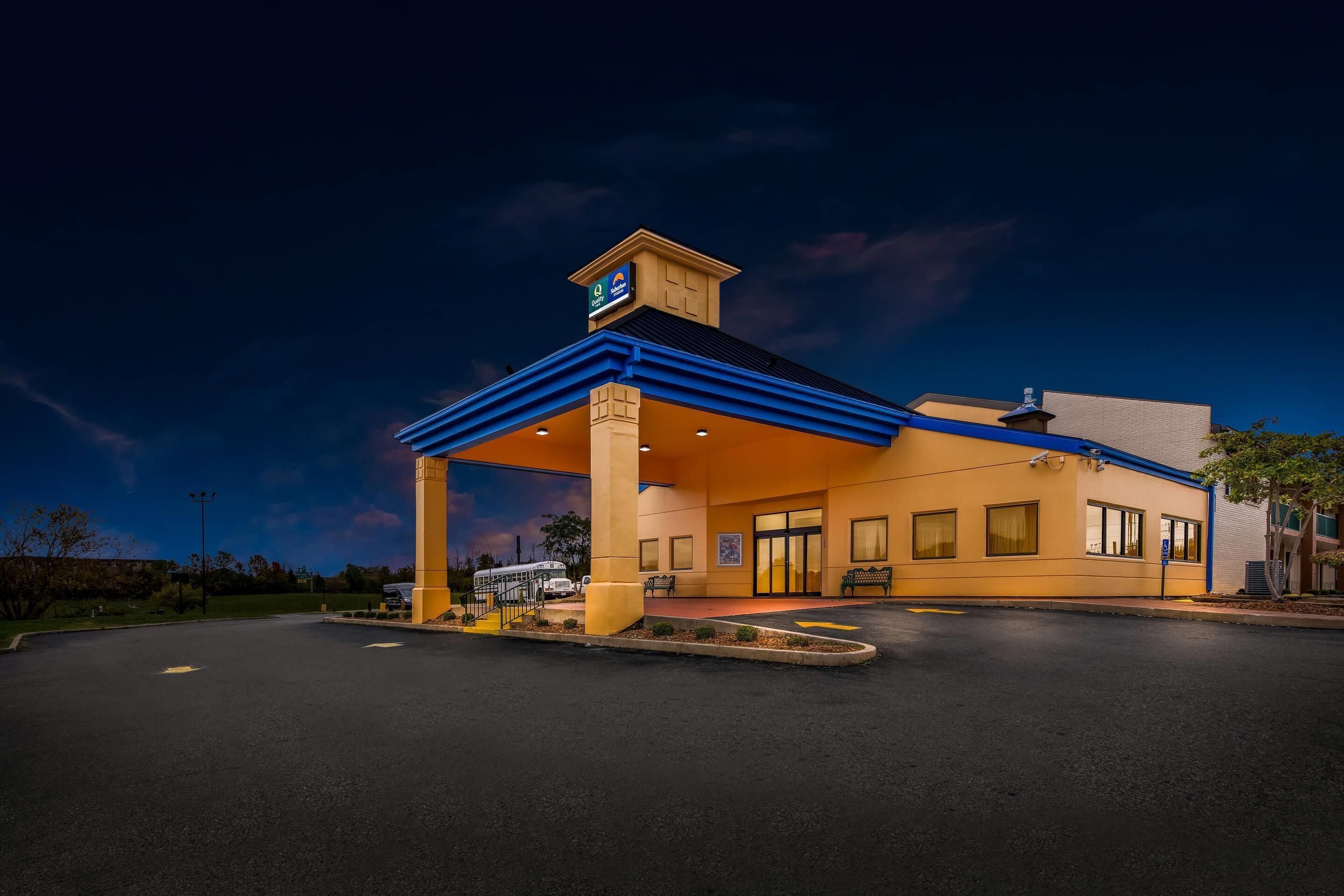 A hotel with a covered outdoor area, a parking lot, and a building with a blue roof.