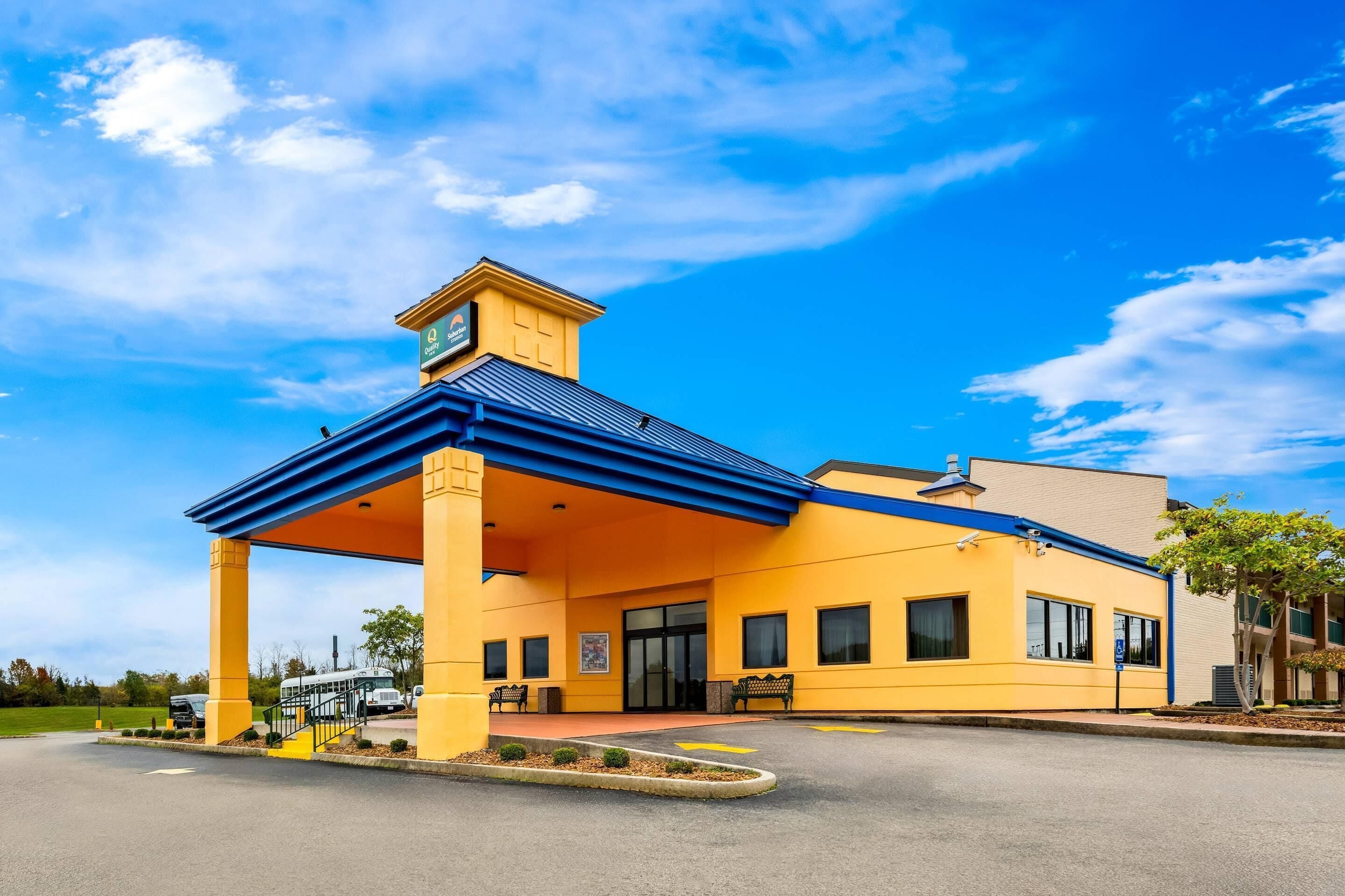 Un bâtiment jaune avec un toit bleu, une entrée couverte et une enseigne indiquant qu’il s’agit d’un hôtel.