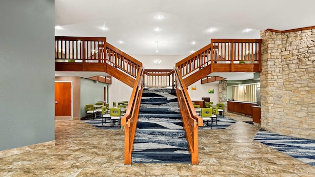 A hotel lobby with a central staircase, multiple dining areas, and a stone accent wall. - Quality Inn Mason Near Kings Island (Mason)